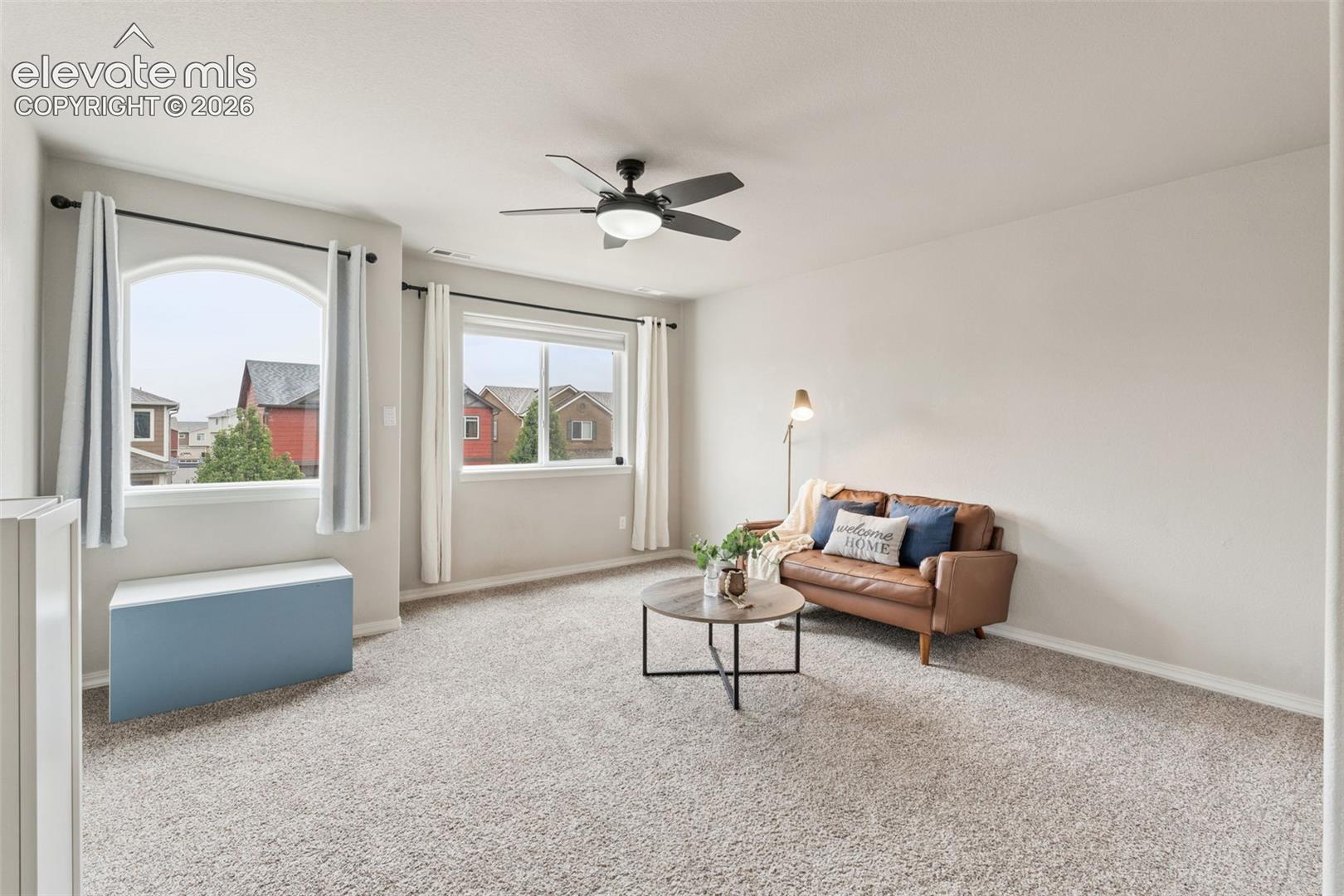 Plush carpet flooring, multiple windows providing natural light, arched window, ceiling fan with integrated lighting, and neutral wall tones