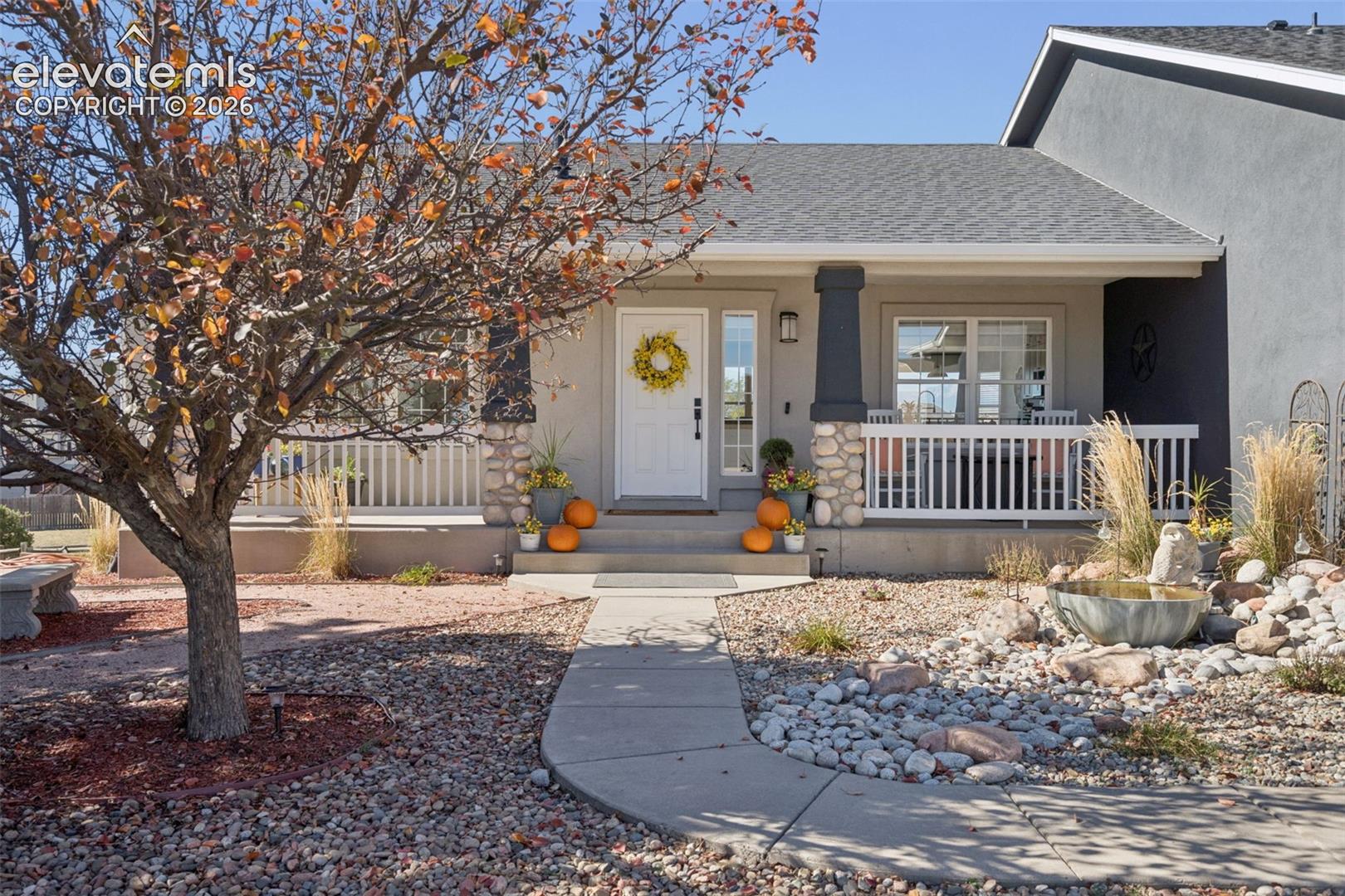 Covered front porch with column supports, white balusters, and a stone base