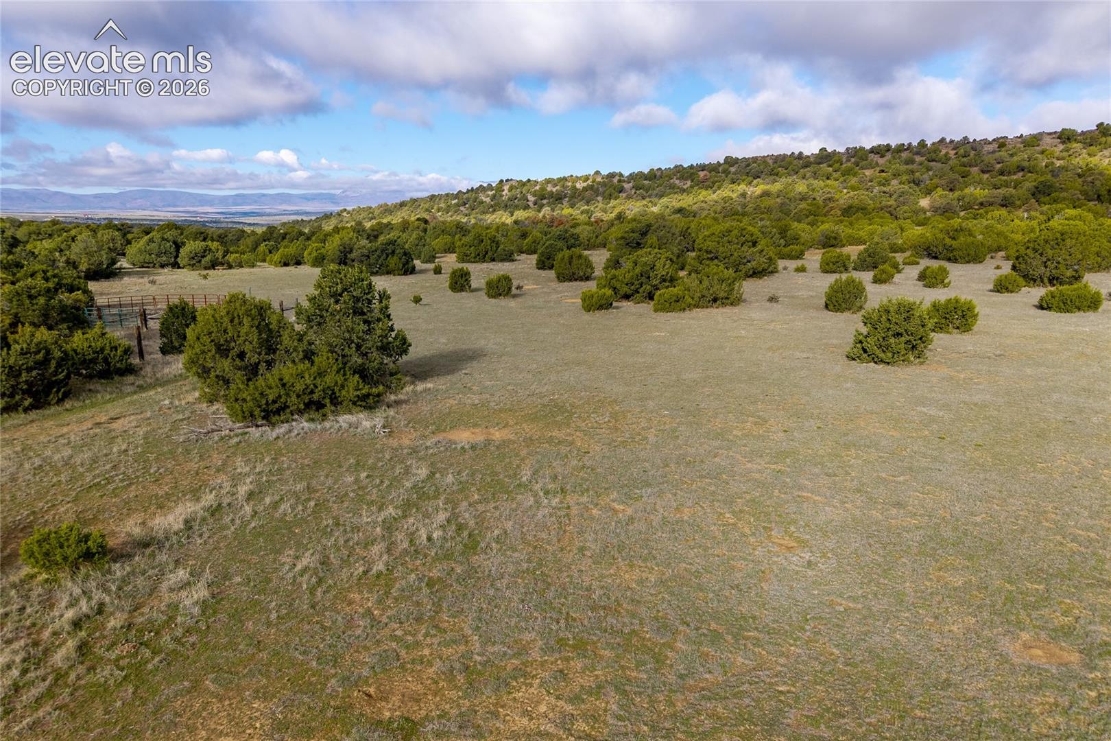 Expansive acreage featuring rolling terrain, native shrubs, mature trees, and wire perimeter fencing