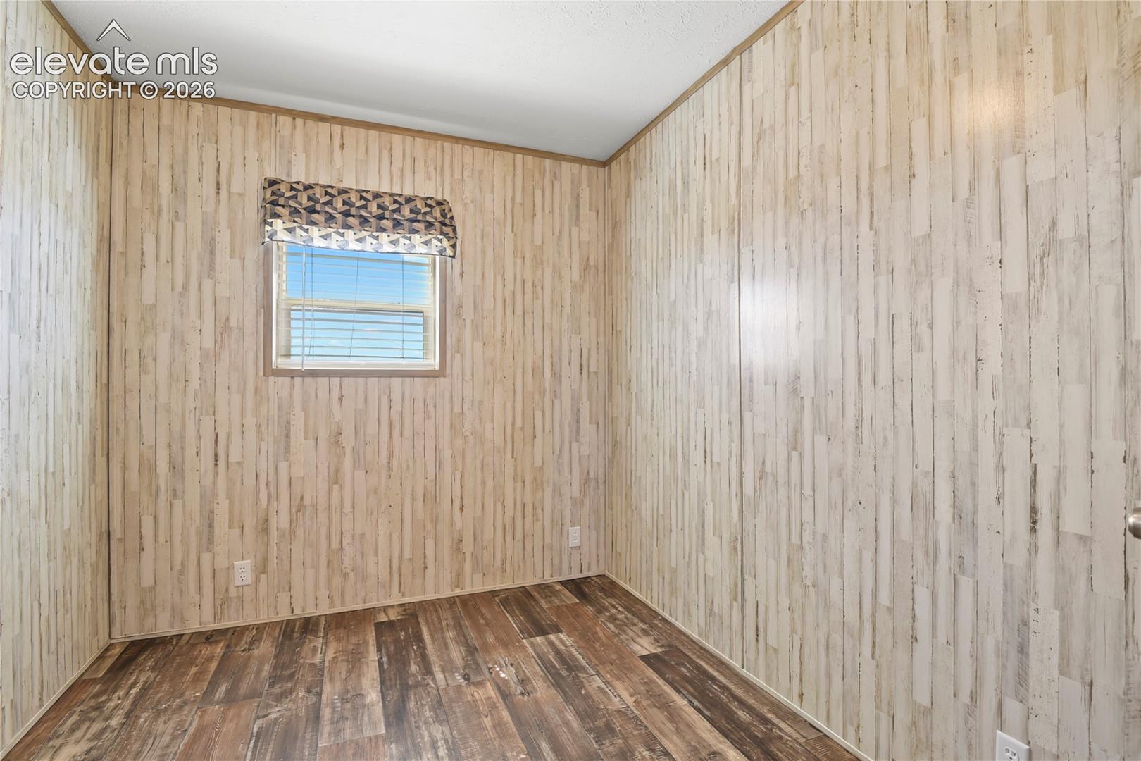 Interior room featuring wood-finish flooring and vertical wood-grain paneled walls with a single horizontal window