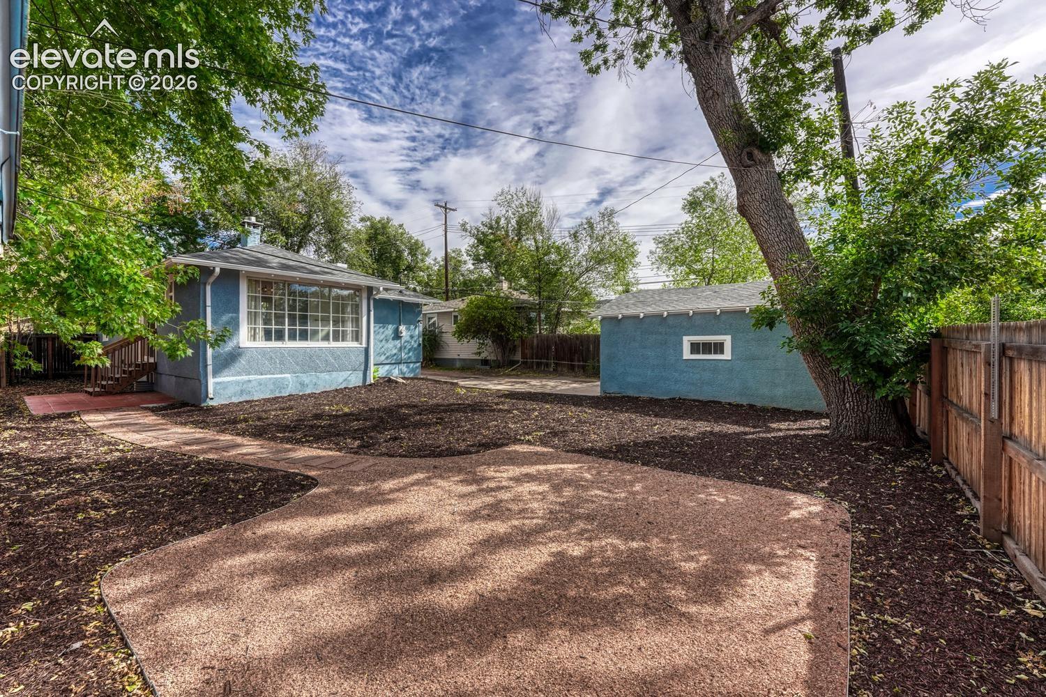 Expansive backyard with a large patio area, mature trees, wood fencing, and a detached structure