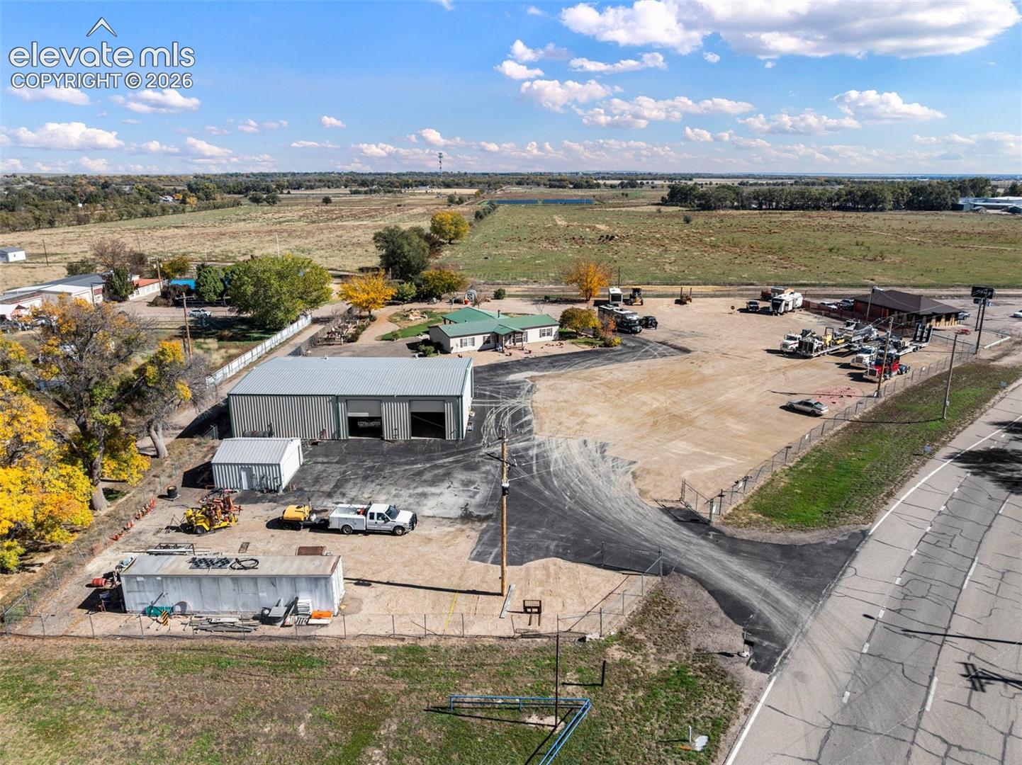 Expansive lot featuring a metal-sided workshop with multiple bays, secondary storage structure, paved parking area, and perimeter chain-link fencing