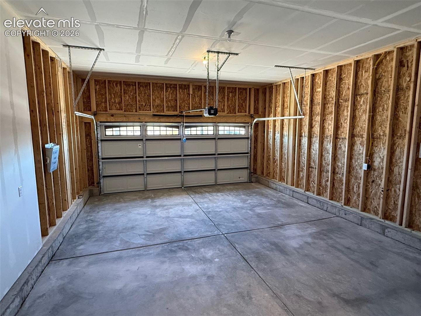 Spacious garage featuring a concrete floor, exposed wood framing, and a segmented garage door with transom windows