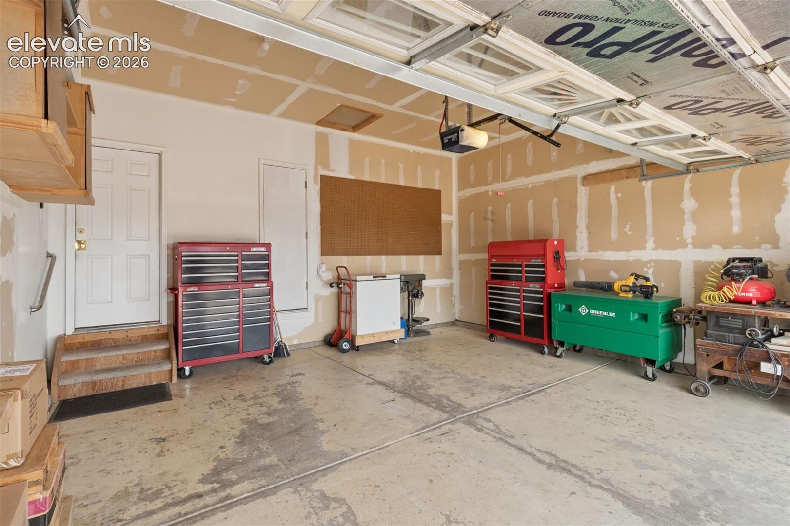 Multi-car garage featuring a concrete floor, overhead door, attic access, and wood-framed stairs