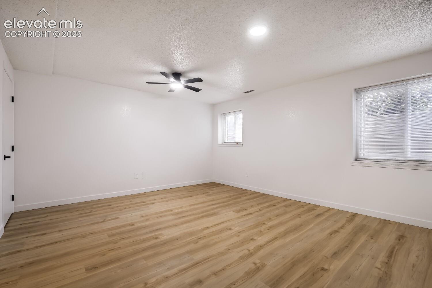 Wood-finish flooring, dual windows, matte black ceiling fan with integrated lighting, and neutral wall tones