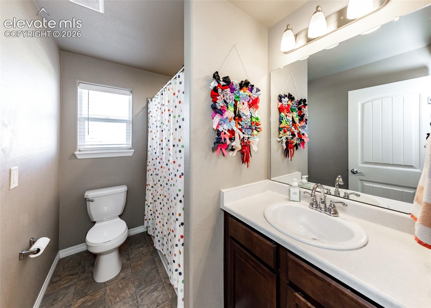 Bathroom featuring a single-sink vanity with a solid-surface countertop, dark wood-finish cabinetry, a large wall-mounted mirror, and tile flooring