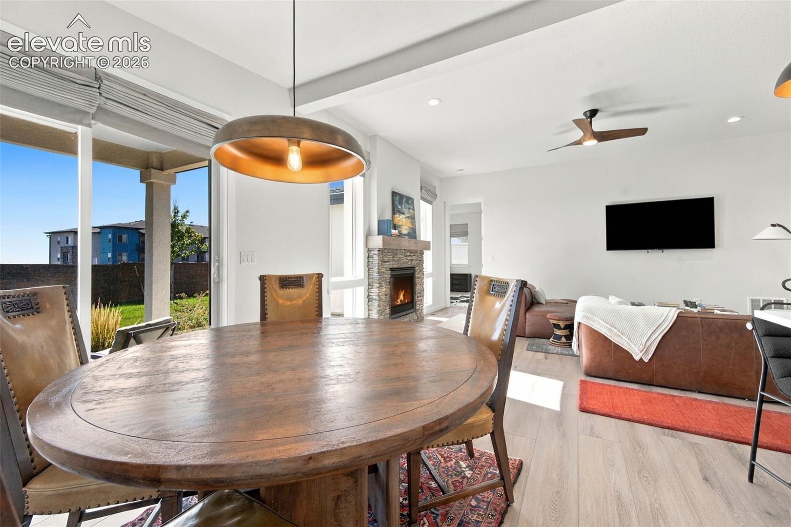 Open-concept interior featuring wood-finish flooring, stone-surround fireplace, large sliding glass doors, modern pendant lighting, and a ceiling fan