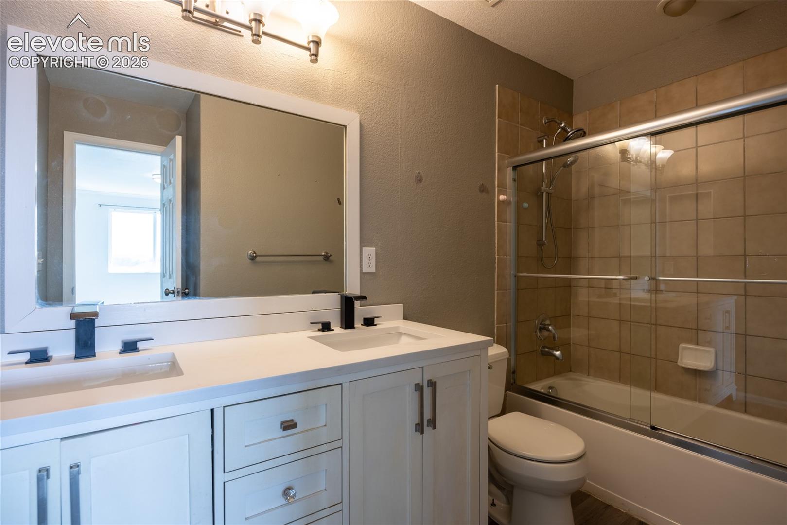 Dual vanity with integrated sinks and black-finish faucets, white shaker-style cabinetry, and a large framed mirror