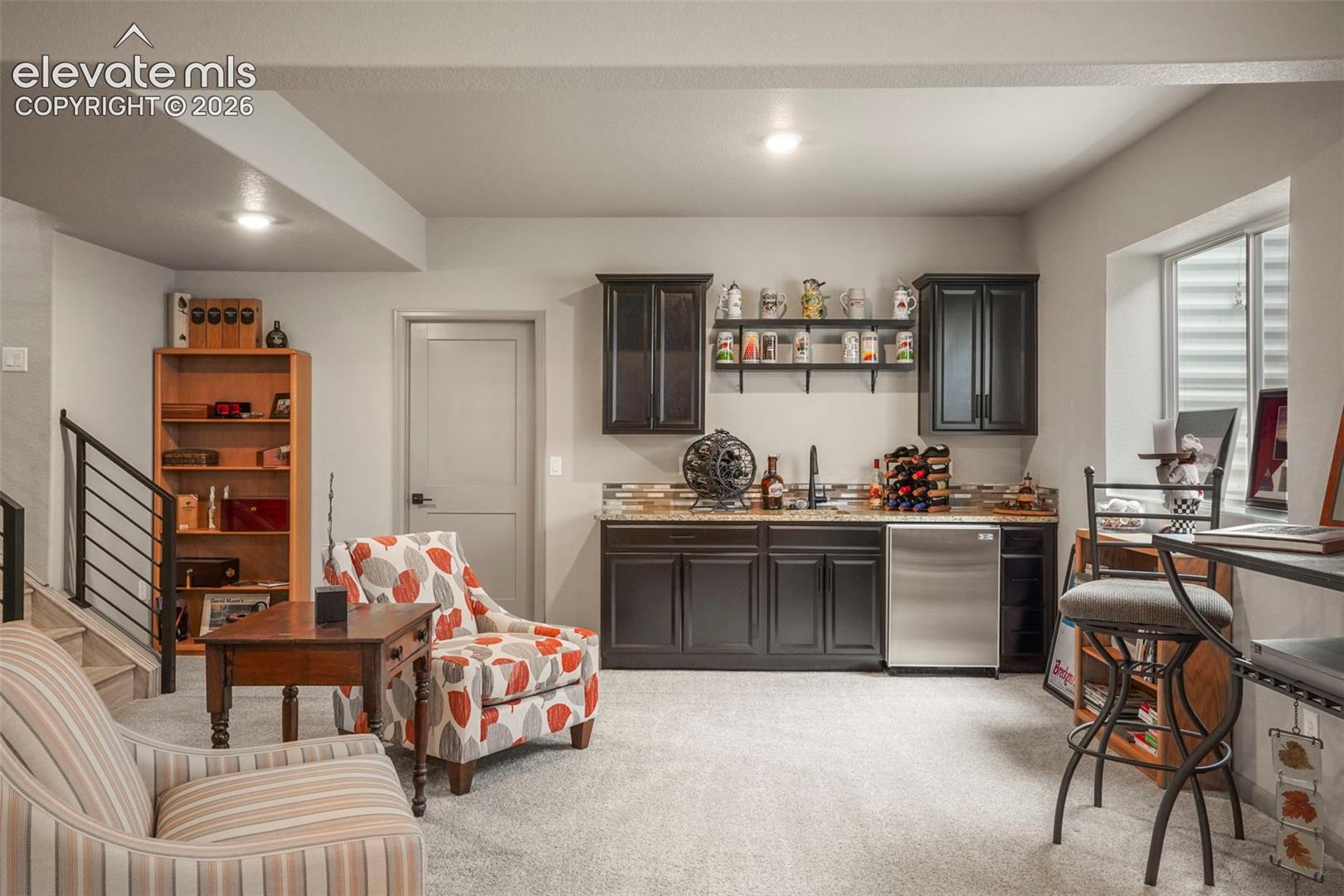 Lower-level recreation space featuring a built-in wet bar with dark cabinetry, stainless steel sink, and beverage refrigerator