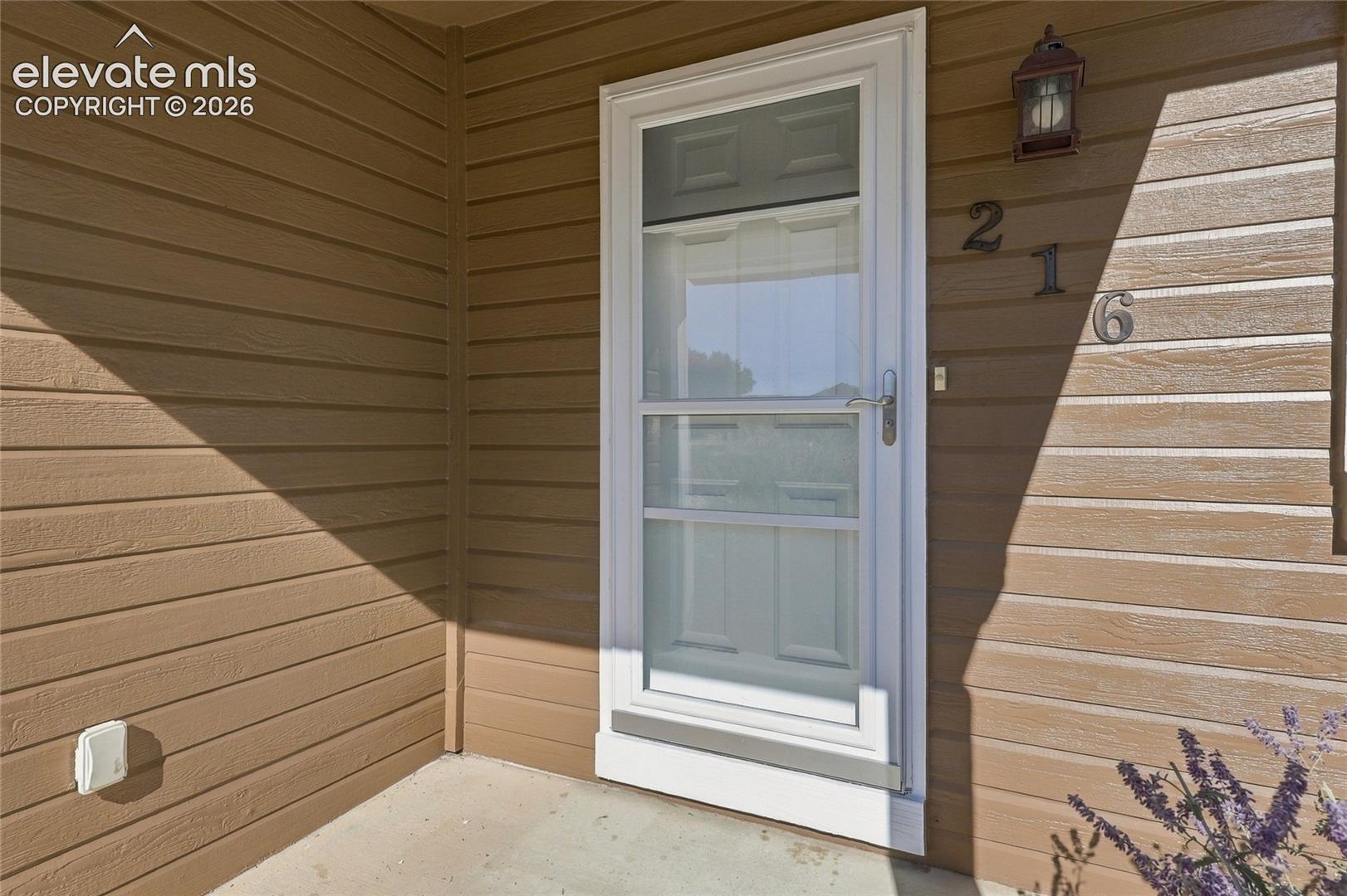 Exterior entry featuring horizontal lap siding, a full-view storm door, and an attached carriage-style light fixture