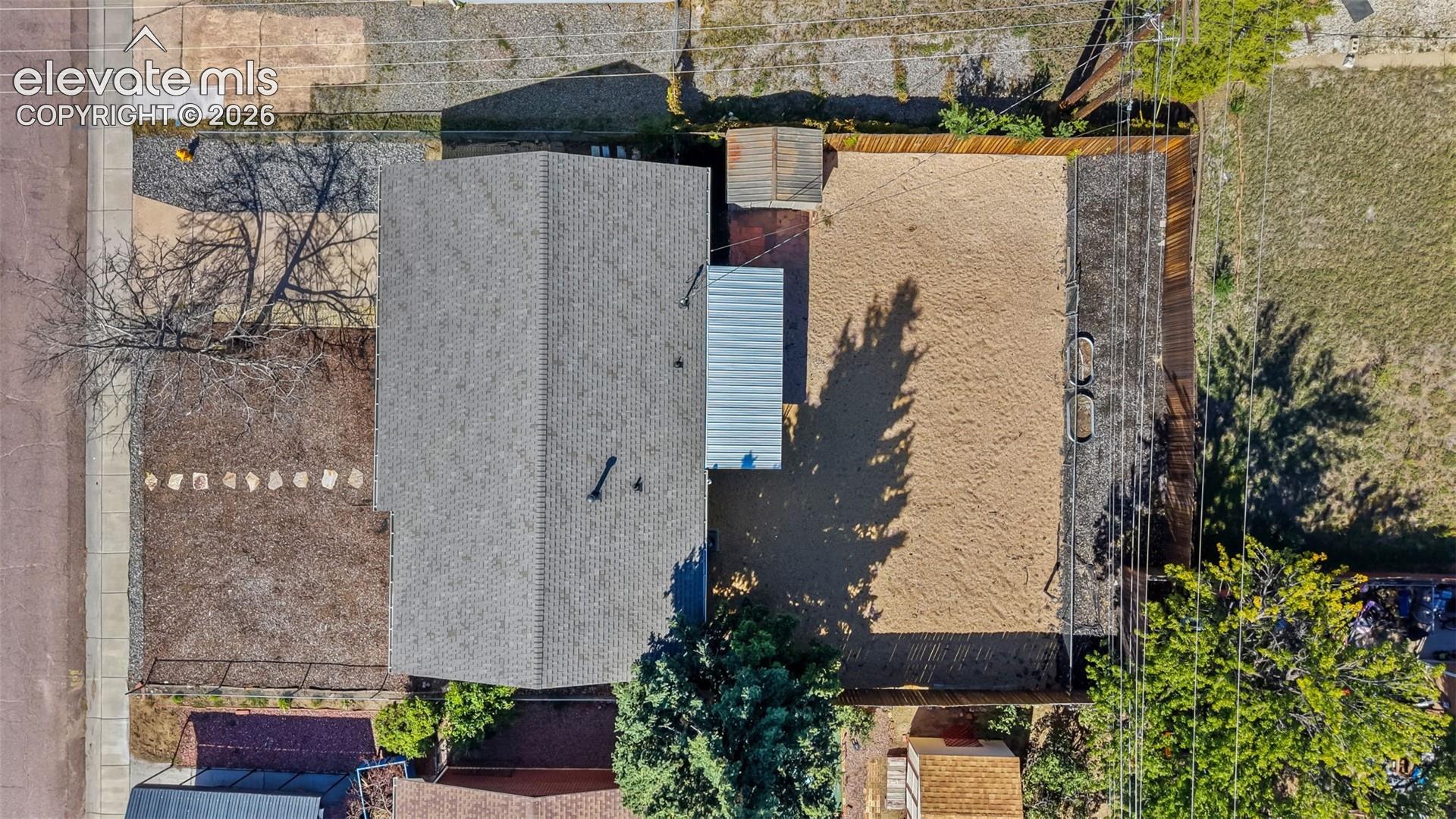 Property with a gray shingle roof, attached metal awning, wood privacy fence, and gravel lot