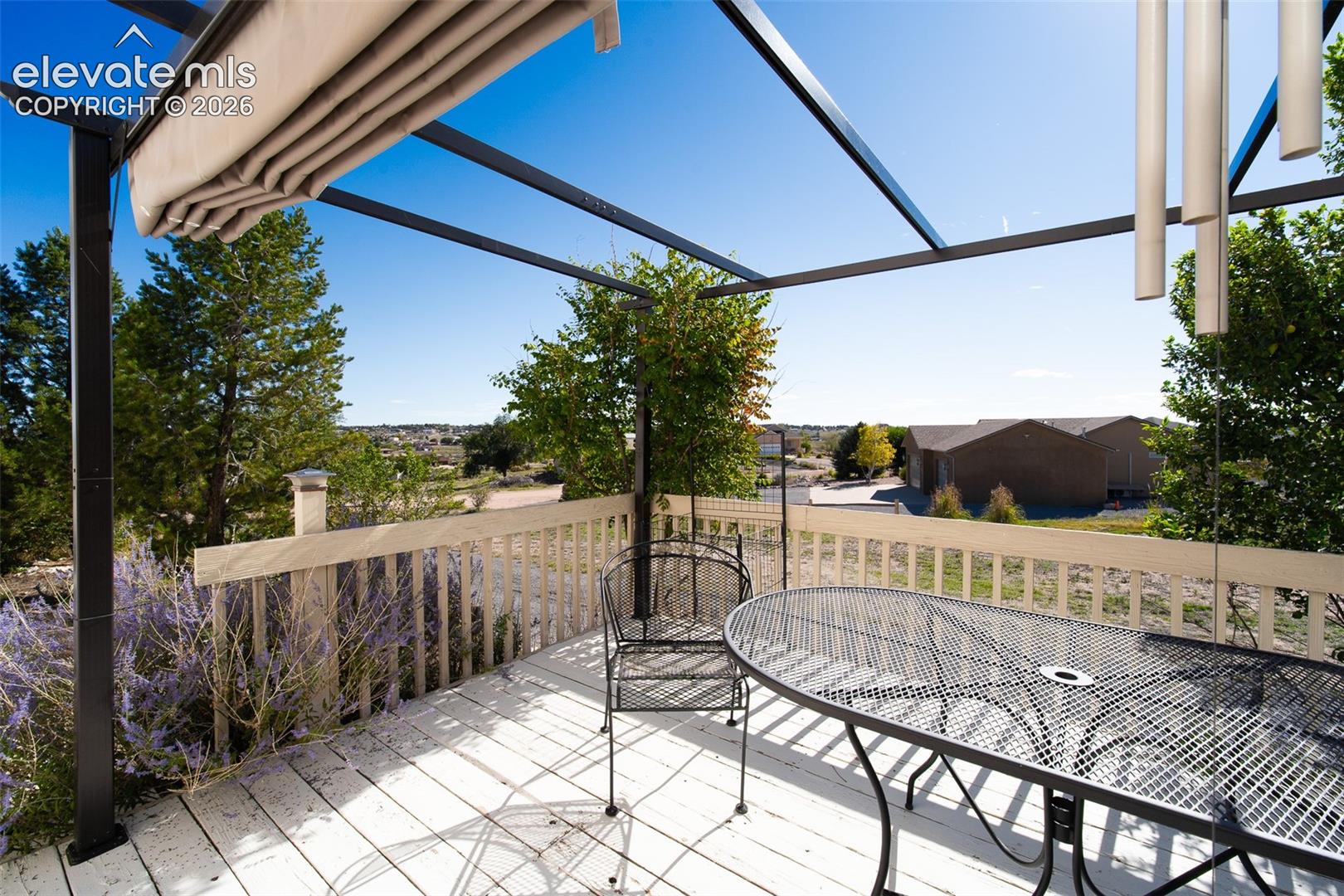 Elevated wood-plank deck featuring a metal pergola with a retractable canopy and a wooden railing