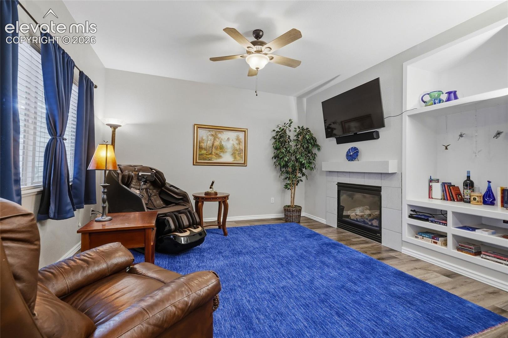 Living area featuring wood-finish flooring, a ceiling fan, and a fireplace with a mantel