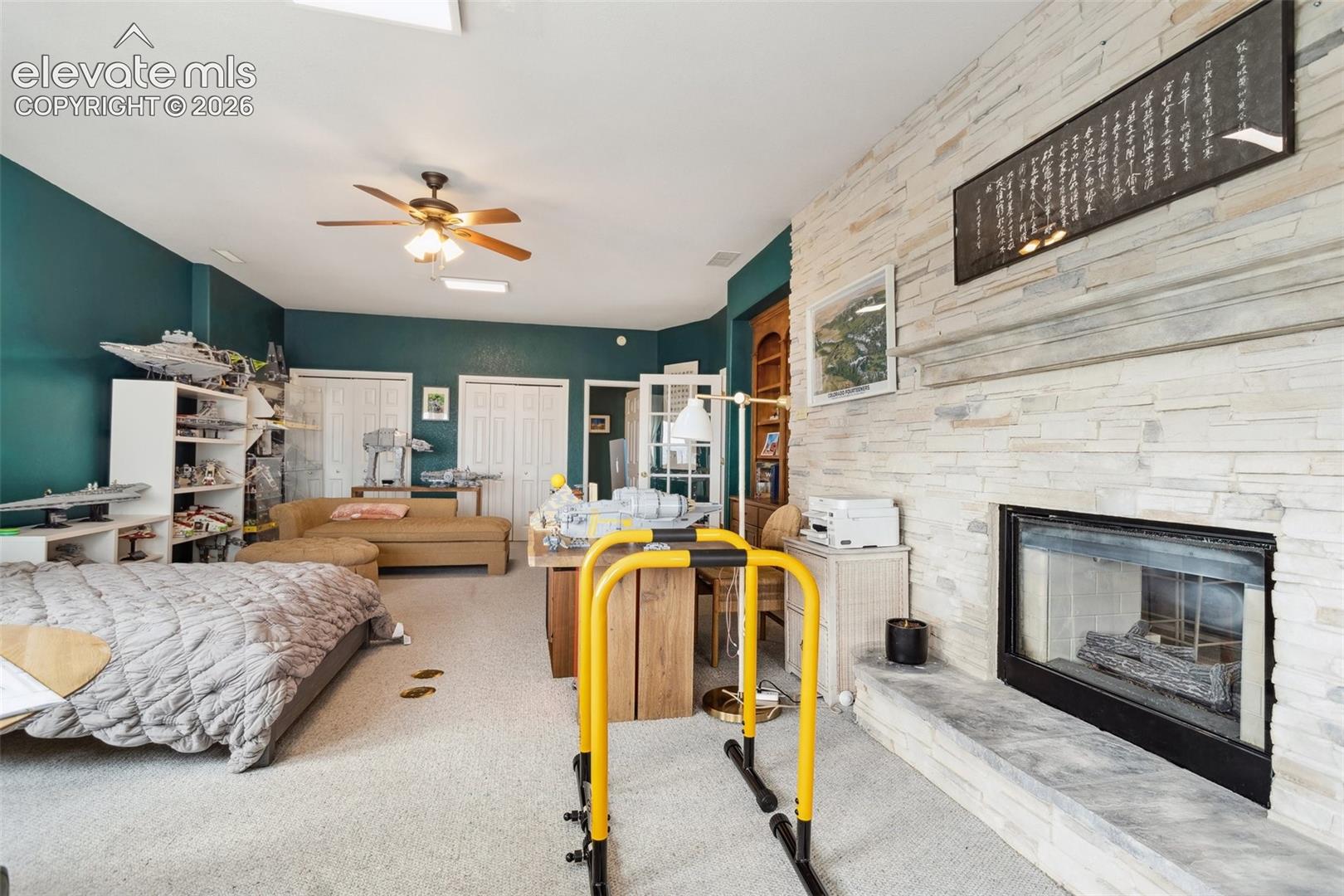 Living area featuring a floor-to-ceiling stacked stone fireplace, a ceiling fan, light gray carpet flooring, and a built-in fireplace with a stone hearth