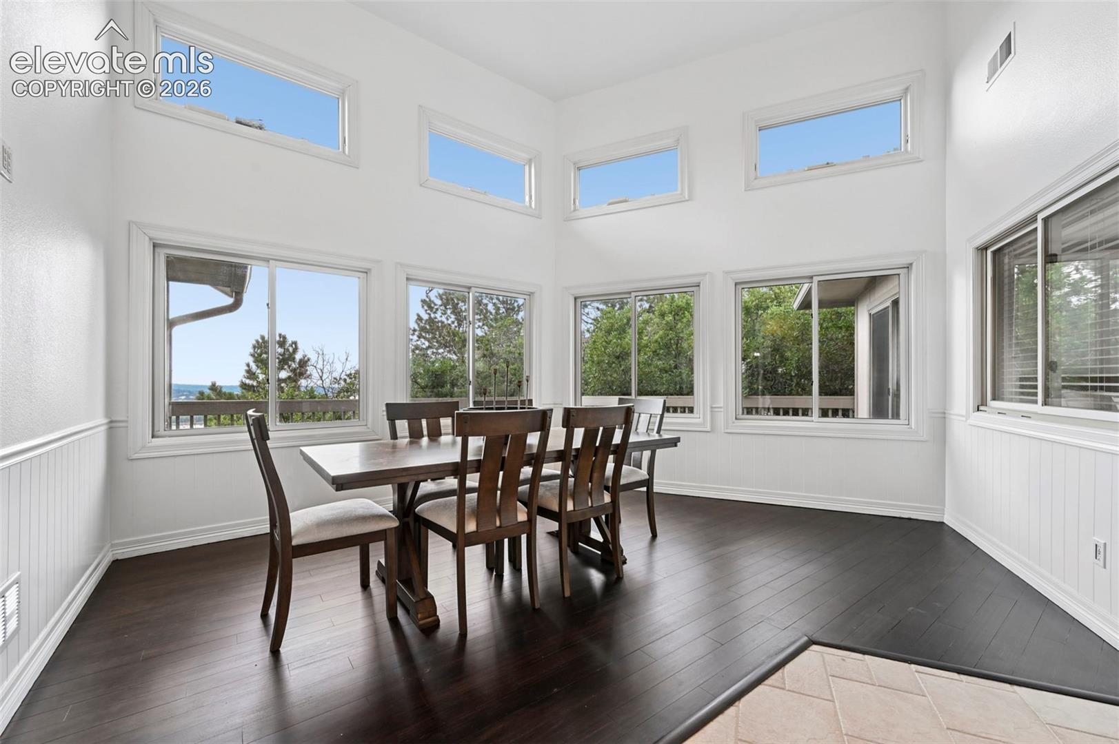 Dining area featuring high ceilings, dark wood-finish flooring, white beadboard wainscoting, and multiple windows