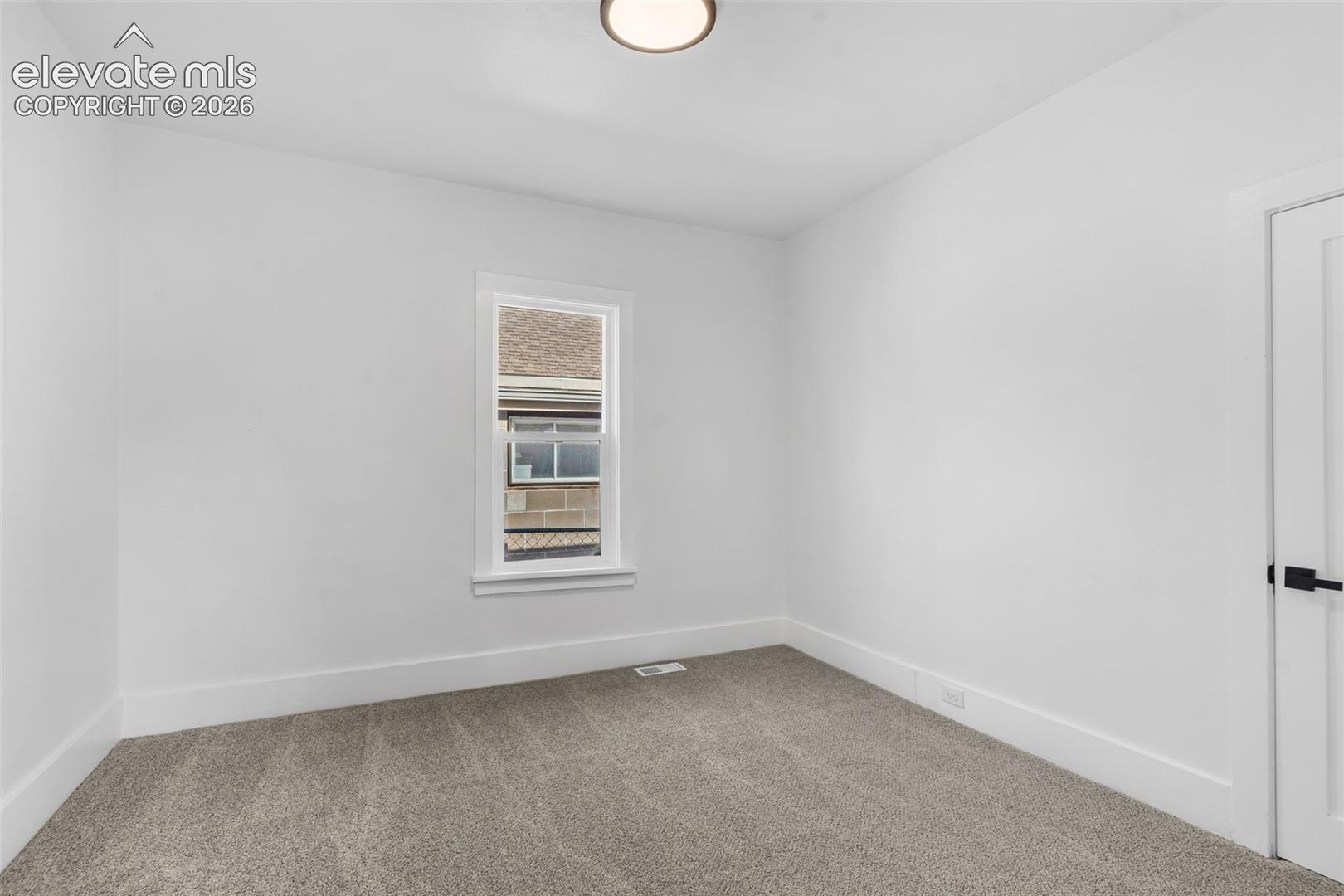 Neutral-toned wall-to-wall carpeting, crisp white wall finish, single-hung window with white casing, and white paneled door with matte black hardware