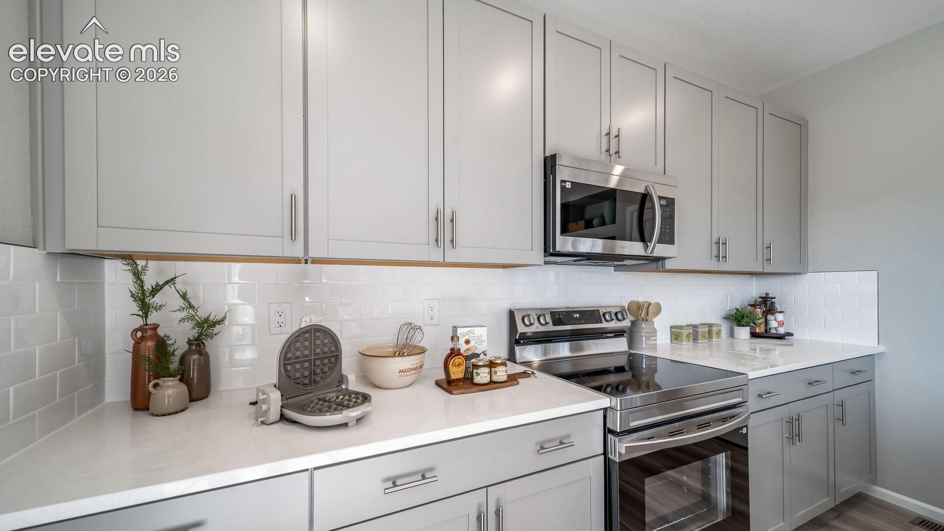Light gray cabinetry with brushed nickel hardware, white stone-finish countertops, subway tile backsplash, and stainless steel appliances
*photos of a model home*