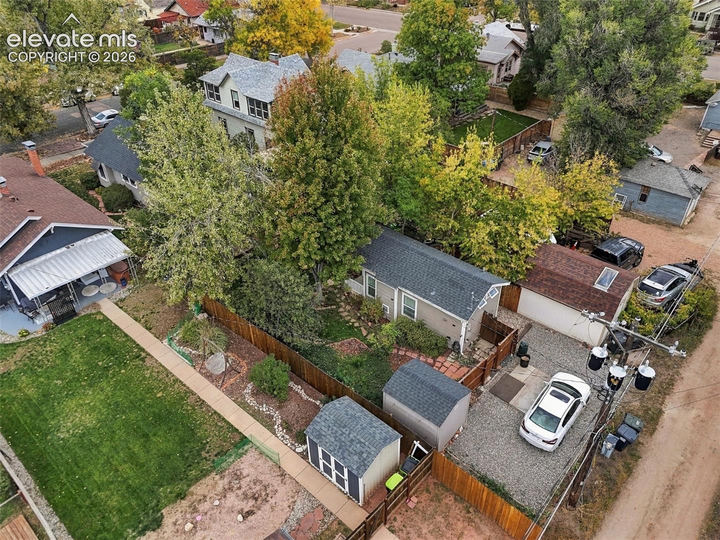 Aerial perspective of a property featuring a detached garage, two external storage structures, a gravel parking area, and wood-panel fencing