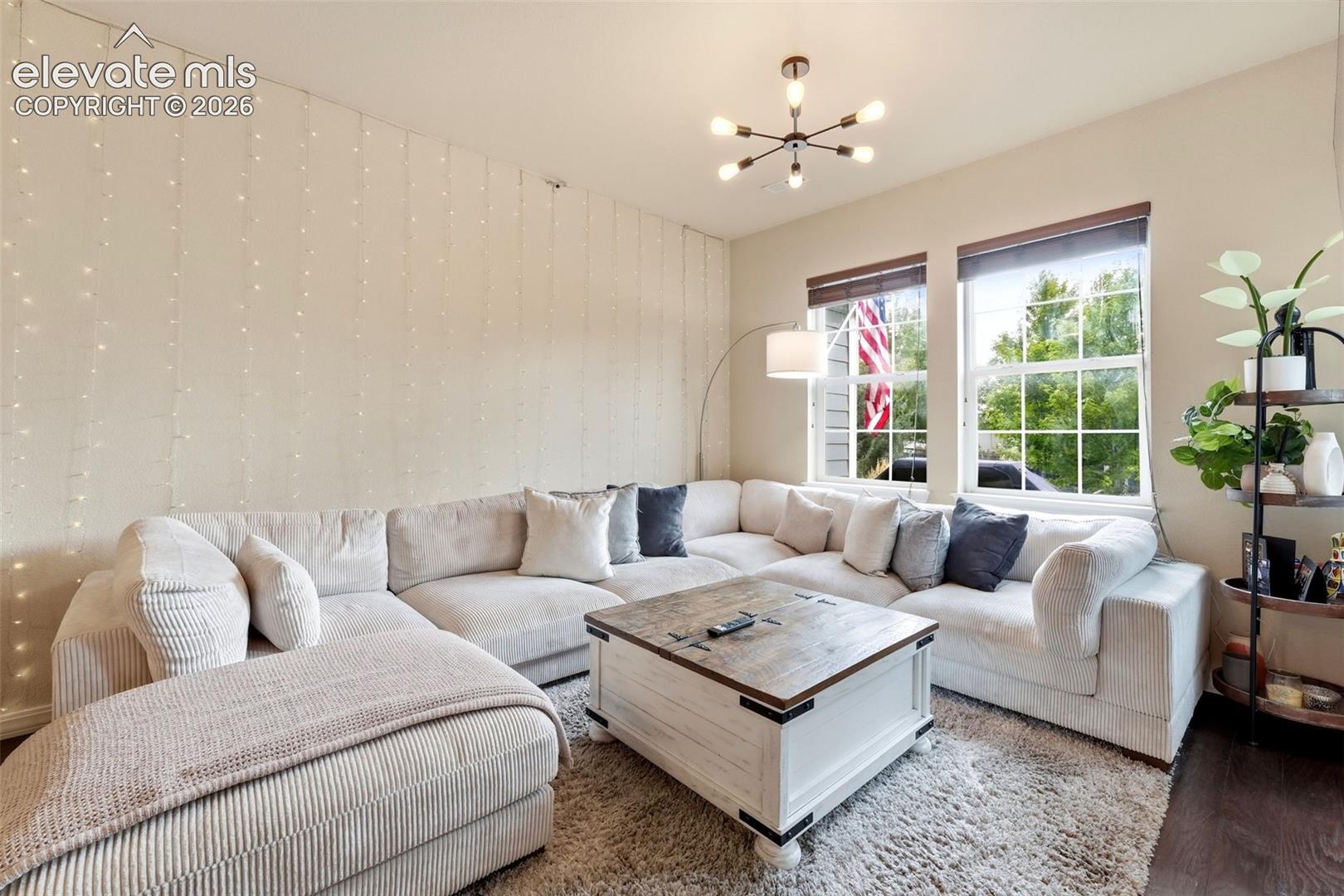 Hardwood-style flooring, dual windows with ample natural light, and a modern chandelier