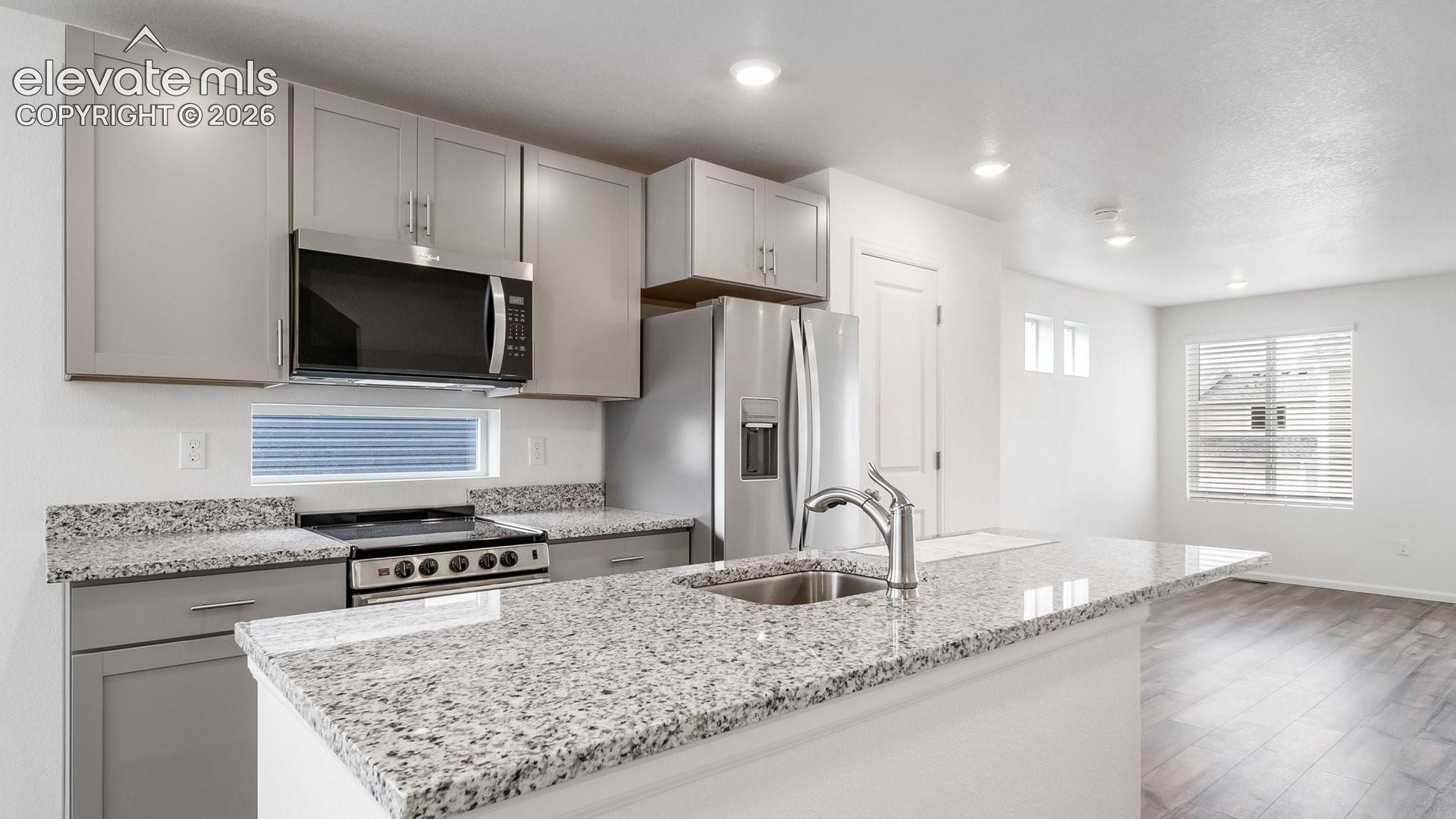 Kitchen featuring light grey cabinetry, stainless steel appliances, granite countertops, and a kitchen island with an undermount sink
*photos of a model home*