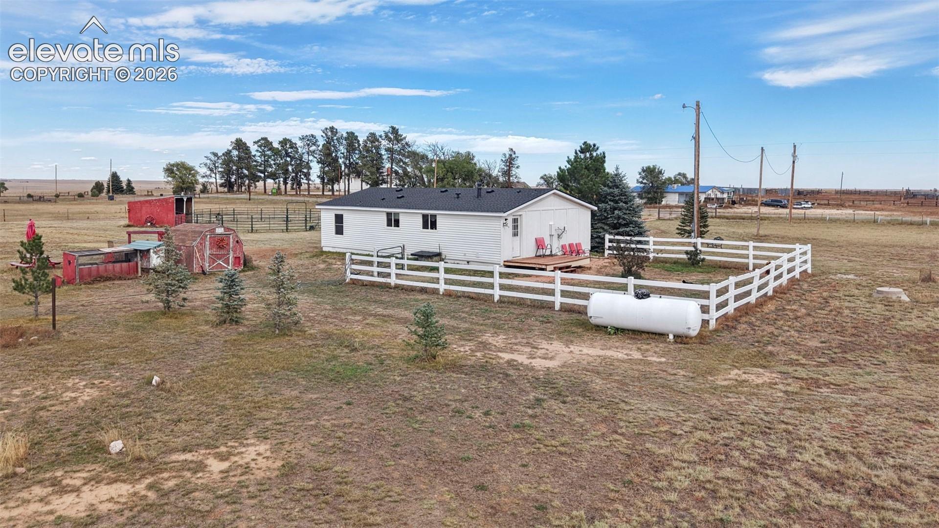 Single-story home featuring a white exterior, white vinyl perimeter fencing, an attached wooden deck, and two detached storage structures situated on 5 acres