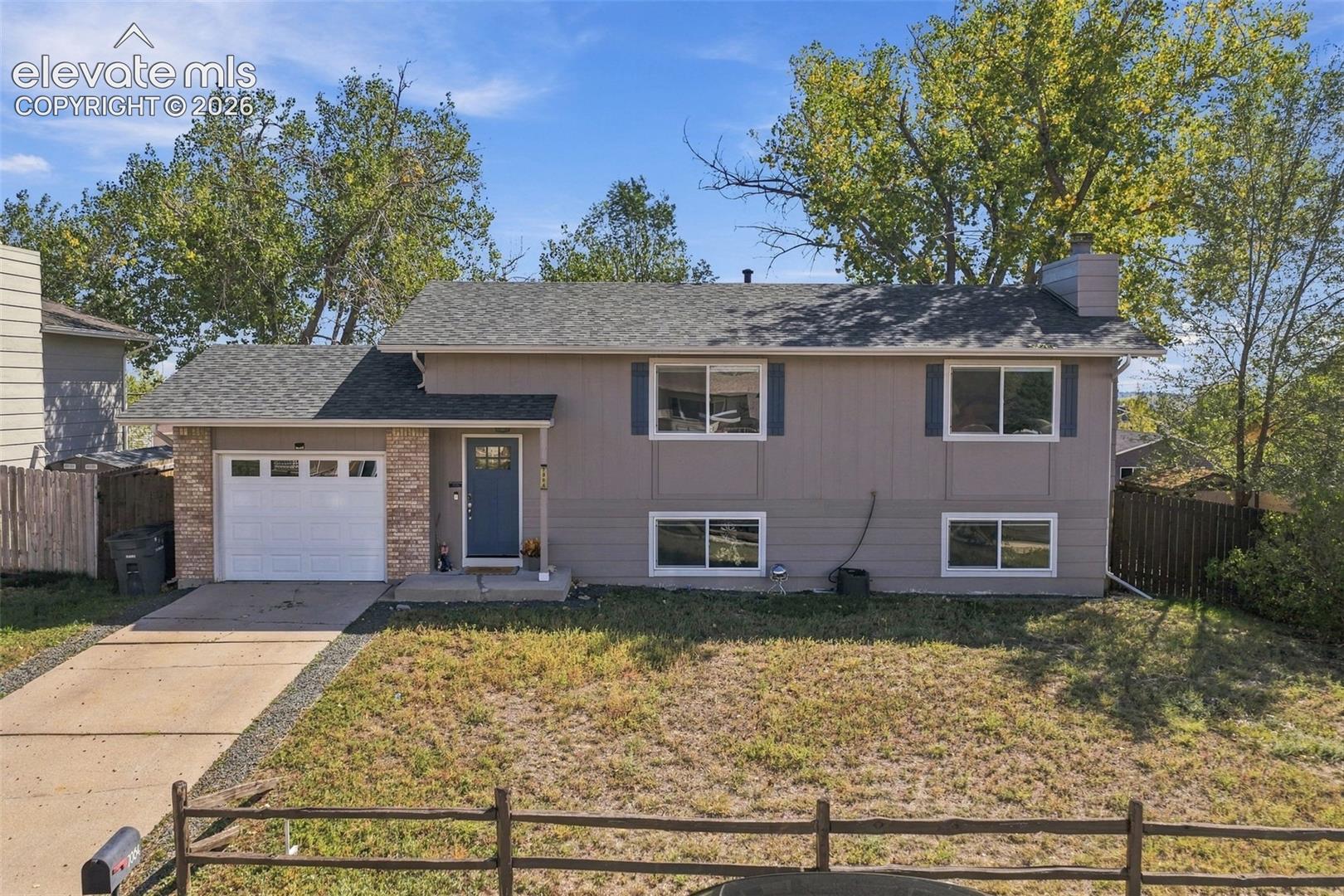 Split-level residence featuring a two-car garage with brick detailing, a concrete driveway, and a front entry door with a storm door