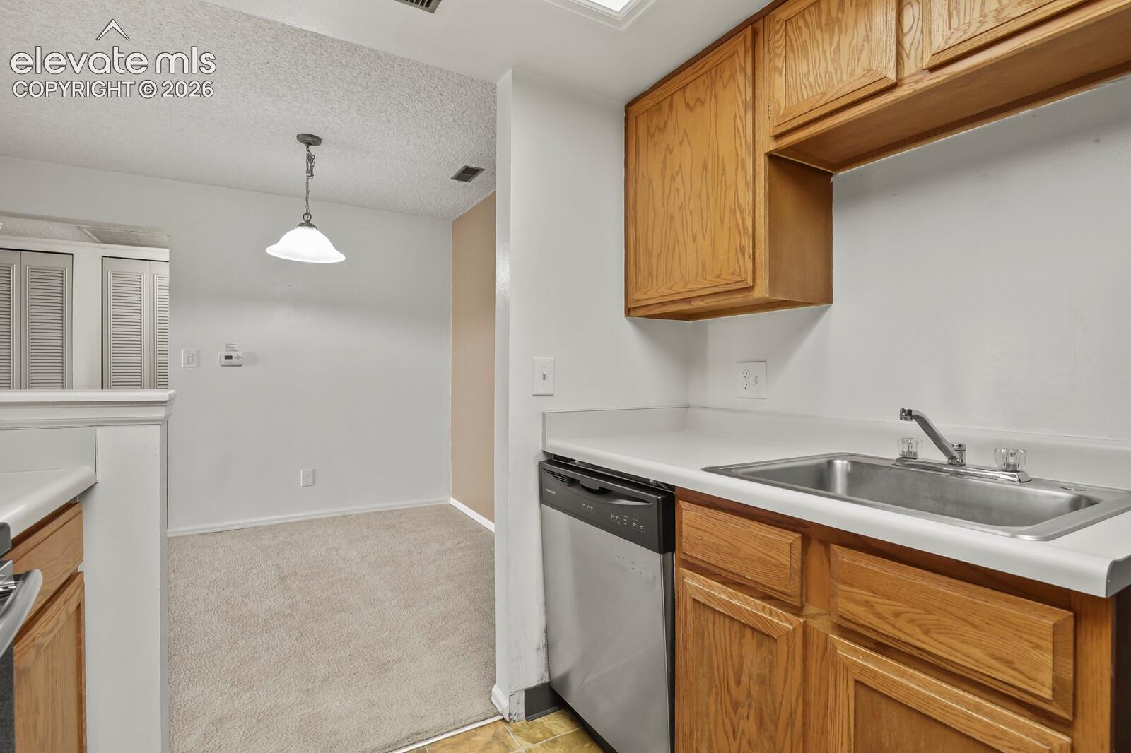 Kitchen featuring wood cabinetry, stainless steel dishwasher, integrated sink, and laminate countertops