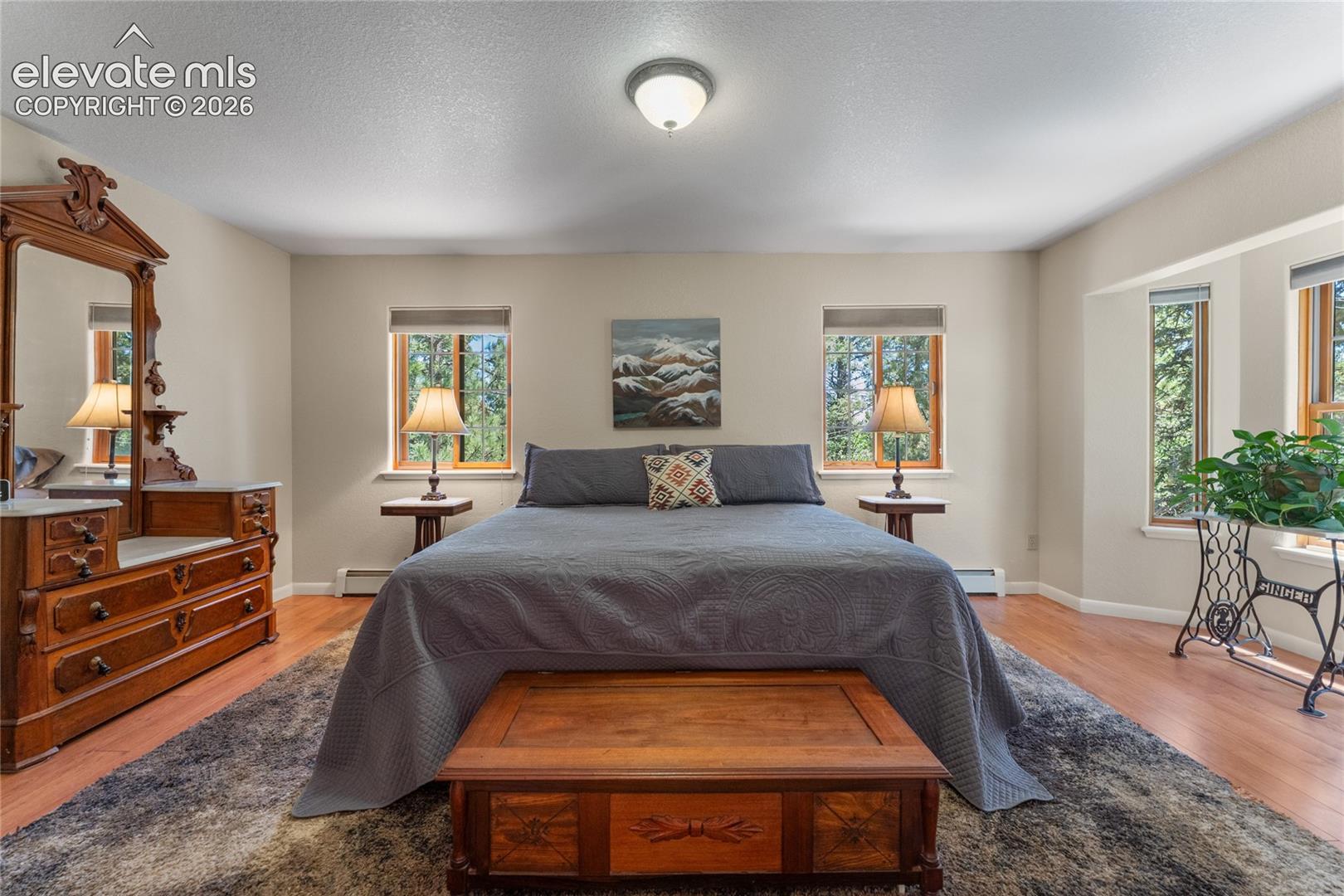 Spacious room featuring wood-finish flooring, light-toned walls, multiple windows with wood trim, and a ceiling-mounted light fixture