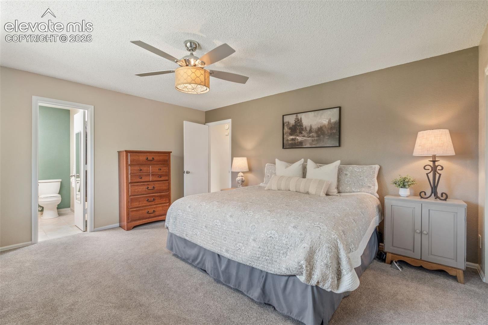 Neutral-toned interior space featuring a ceiling fan with integrated drum light fixture, wall-to-wall carpeting, and a doorway opening to an auxiliary room