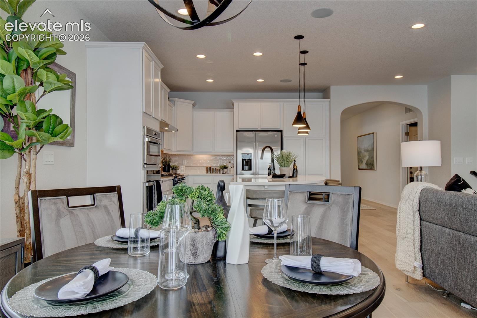 White shaker-style cabinetry, stainless steel built-in appliances, recessed lighting, neutral backsplash, and wood-finish flooring