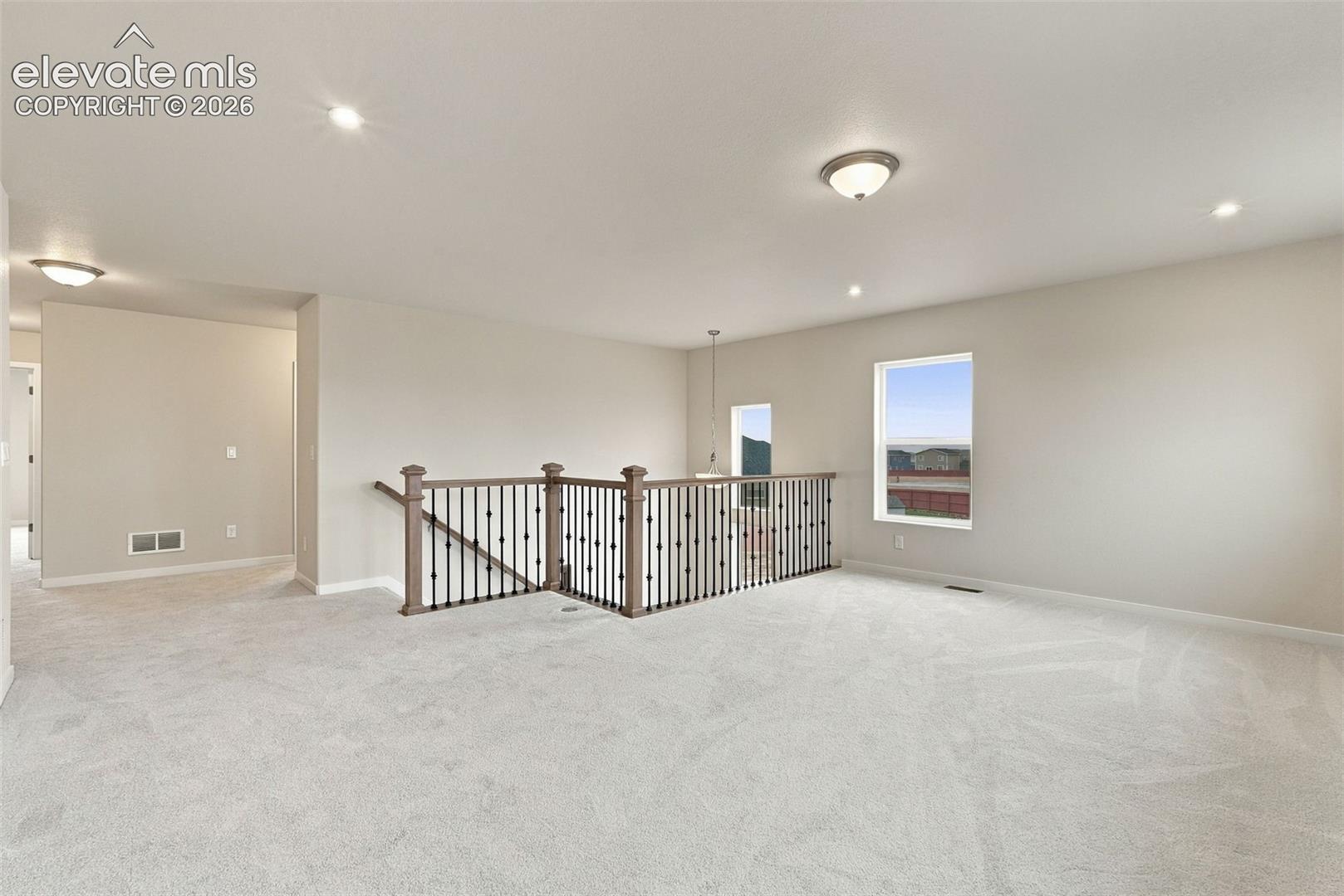 Open floor plan featuring wall-to-wall carpeting, wrought iron balusters with wood-finish handrails, and recessed lighting