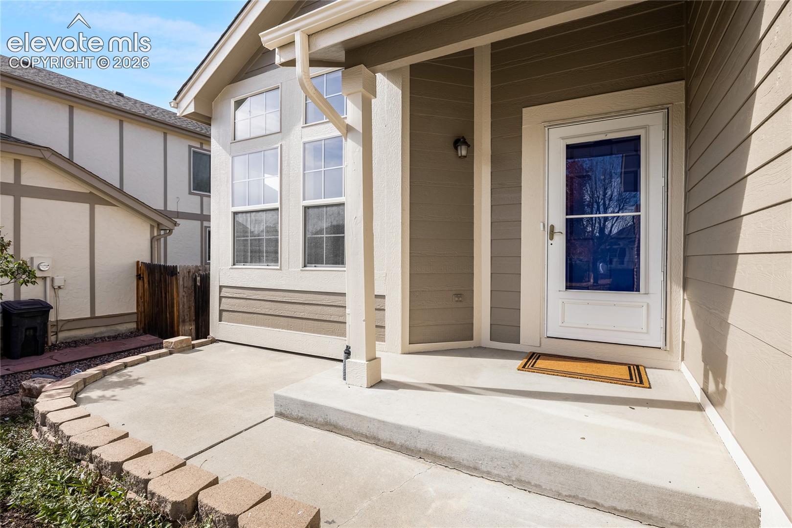 Exterior entrance featuring horizontal lap siding, a concrete porch, stackable stone hardscaping, and a glass-paneled entry door