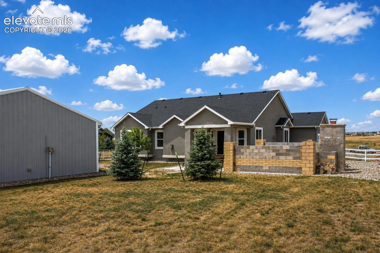 Stucco exterior with a dark shingle roof, accompanied by a detached metal-sided outbuilding