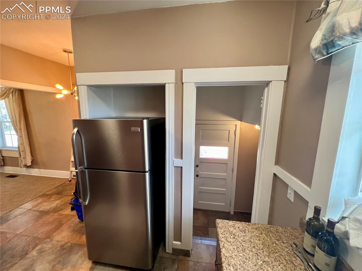 Kitchen with stainless steel refrigerator, an inviting chandelier, dark tile floors, and hanging light fixtures