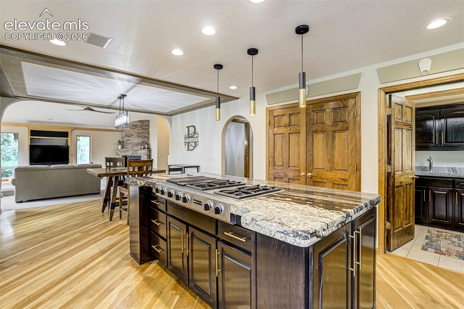Kitchen island with a built-in gas cooktop, granite countertop, recessed lighting, and wood-finish flooring