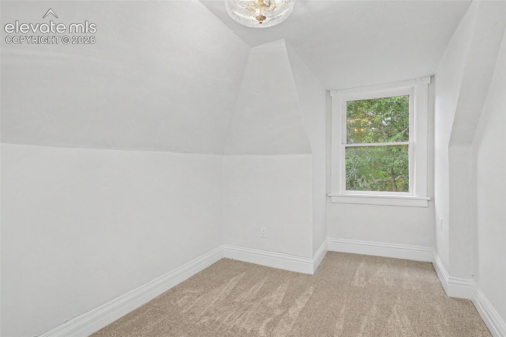 Room featuring sloped ceilings, a single window with white trim, and neutral-toned carpet flooring