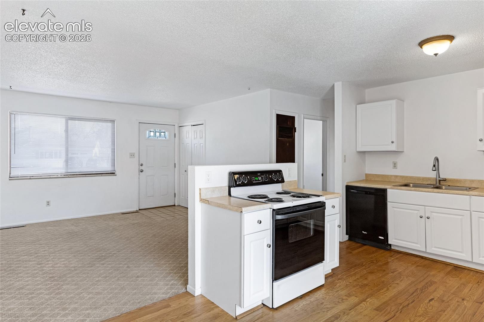Bright kitchen featuring wood-finish flooring, white cabinetry, a black range, and a stainless steel sink with a gooseneck faucet