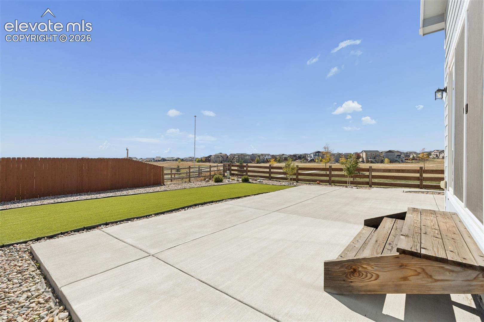 Concrete patio with wooden steps, synthetic turf lawn, wood-style privacy fencing, and stone landscape bordering