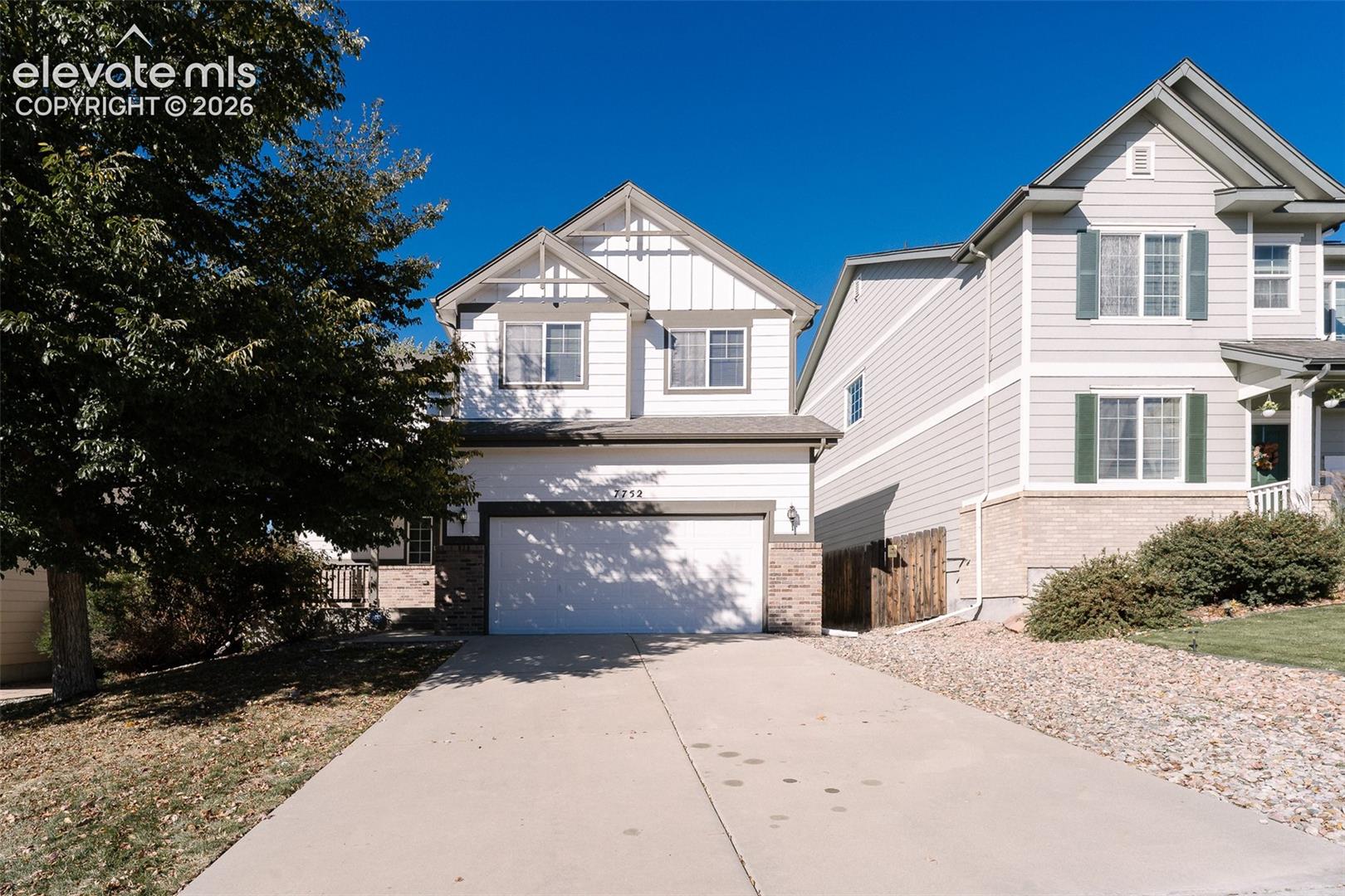Two-story exterior featuring lap siding, vertical board-and-batten gable accents, stone veneer wainscoting, an attached two-car garage, and a concrete driveway