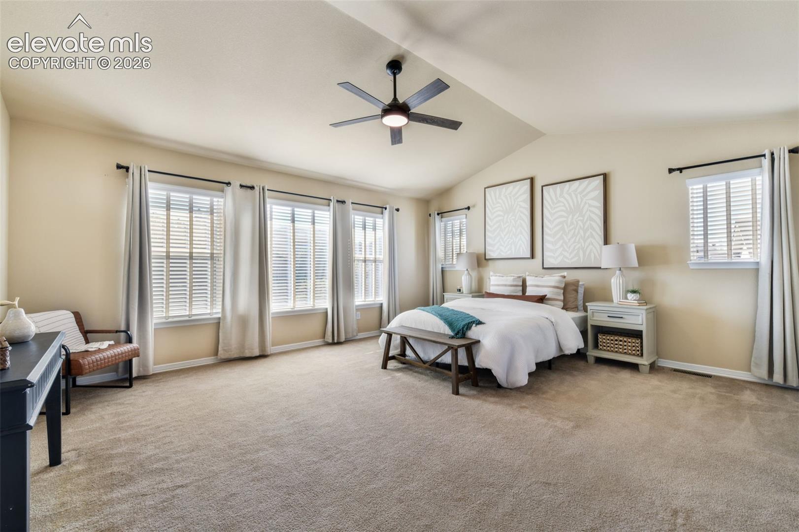 Vaulted ceiling with a ceiling fan, five windows with blinds, and neutral carpeting