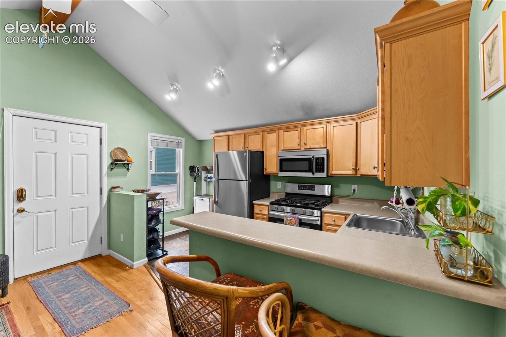 Vaulted ceiling with recessed lighting, wood-finish cabinetry, stainless steel appliances, breakfast bar, and wood-finish flooring