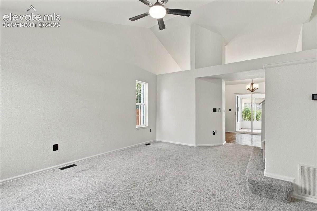 Vaulted ceilings featuring a central ceiling fan with integrated lighting, neutral wall-to-wall carpeting, and a multi-pane window