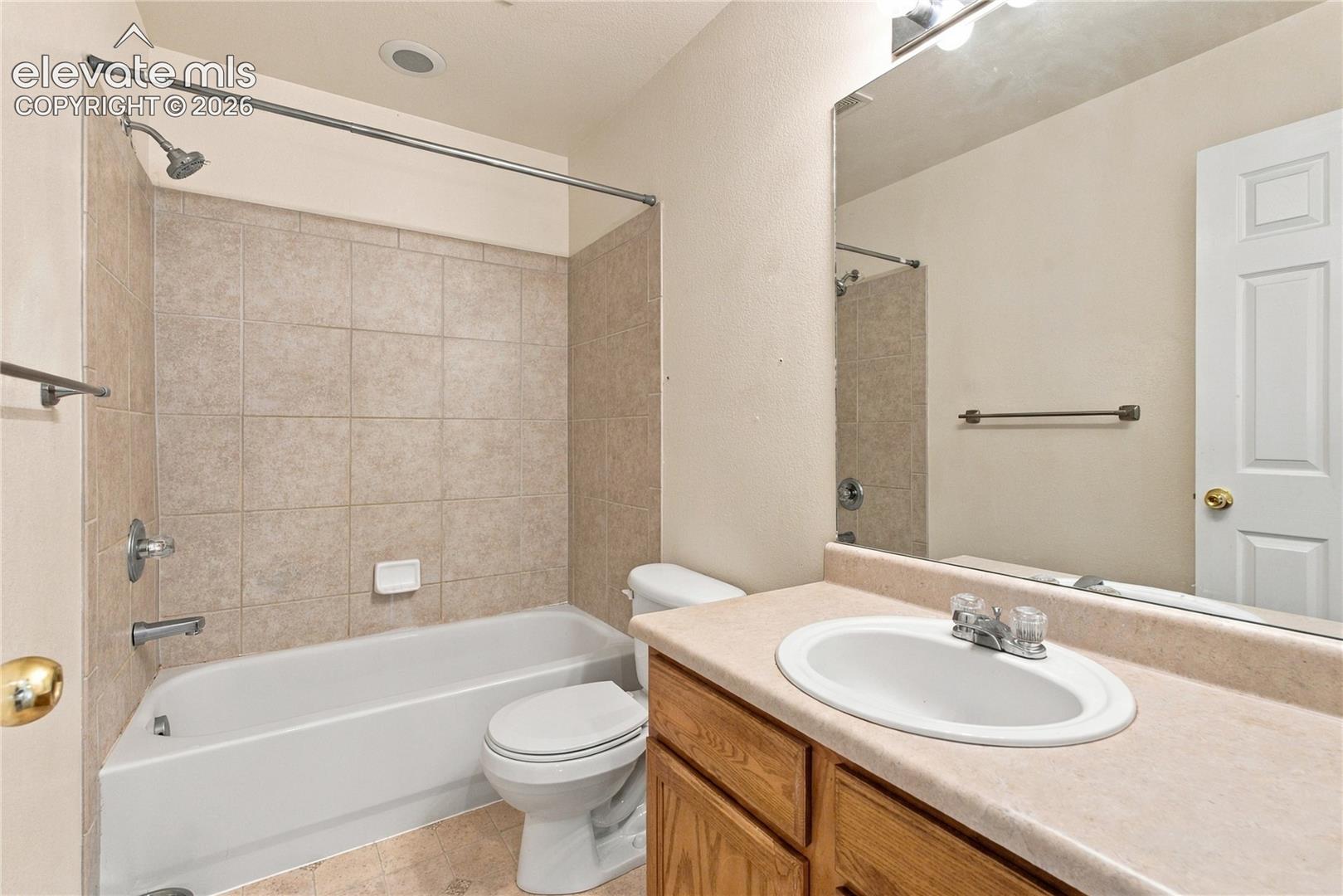 Full bathroom featuring a tub-shower combination with tile surround, wood-finish vanity with an integrated countertop and sink, and a wall-mounted mirror