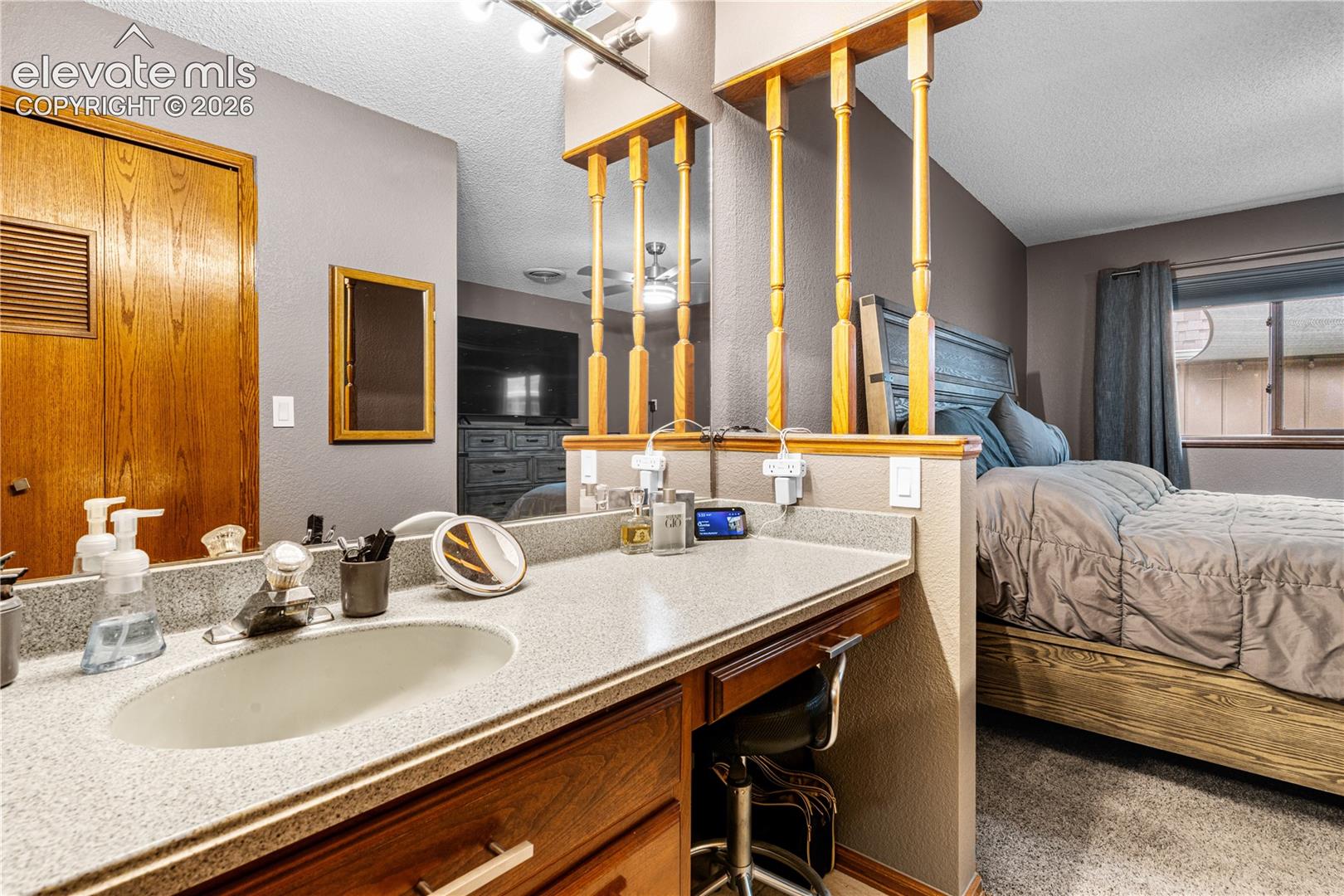 Vanity area featuring wood cabinetry, a solid surface countertop with an integrated oval sink, full-width mirror, and decorative spindle partition