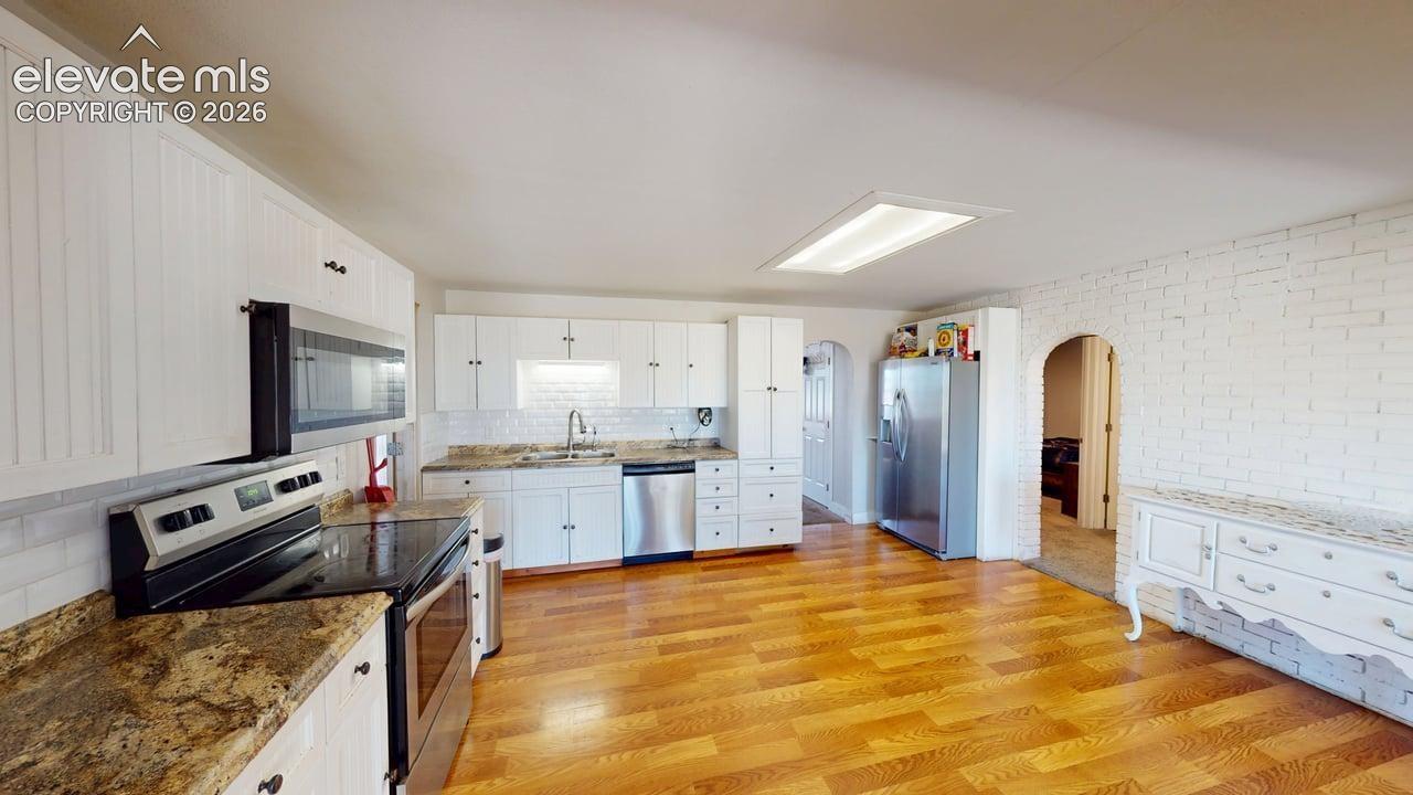 White cabinetry, wood-finish flooring, stainless steel appliances, speckled stone countertops, and a white subway tile backsplash