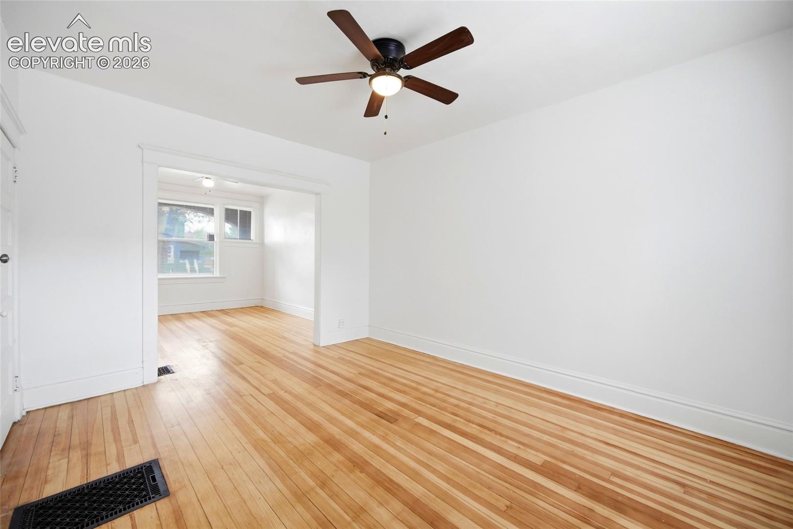 Wood-finish flooring, white walls, and a ceiling-mounted fan with integrated light fixture