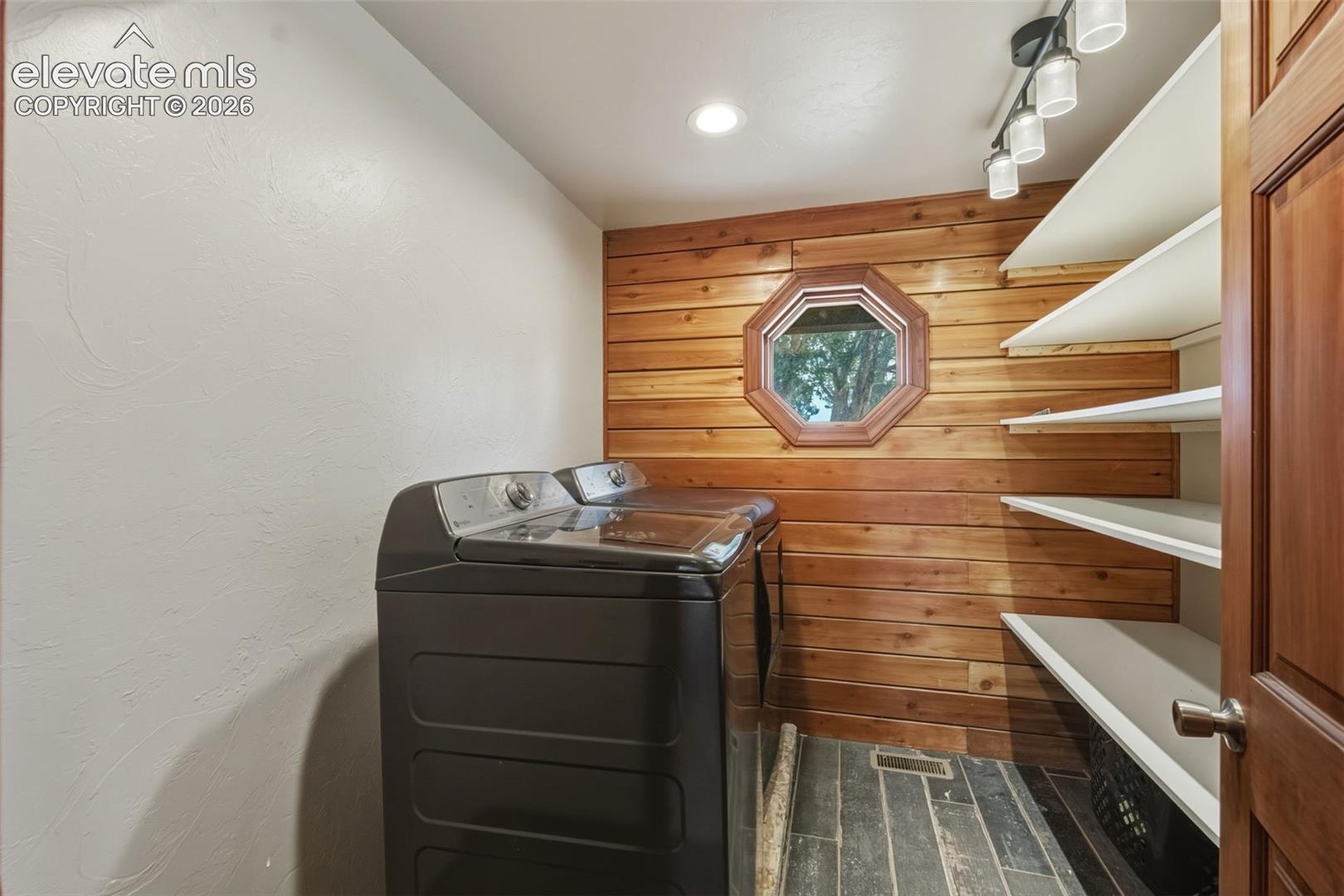 Wood-paneled accent wall with an octagonal window, built-in shelving, track lighting, and tile flooring