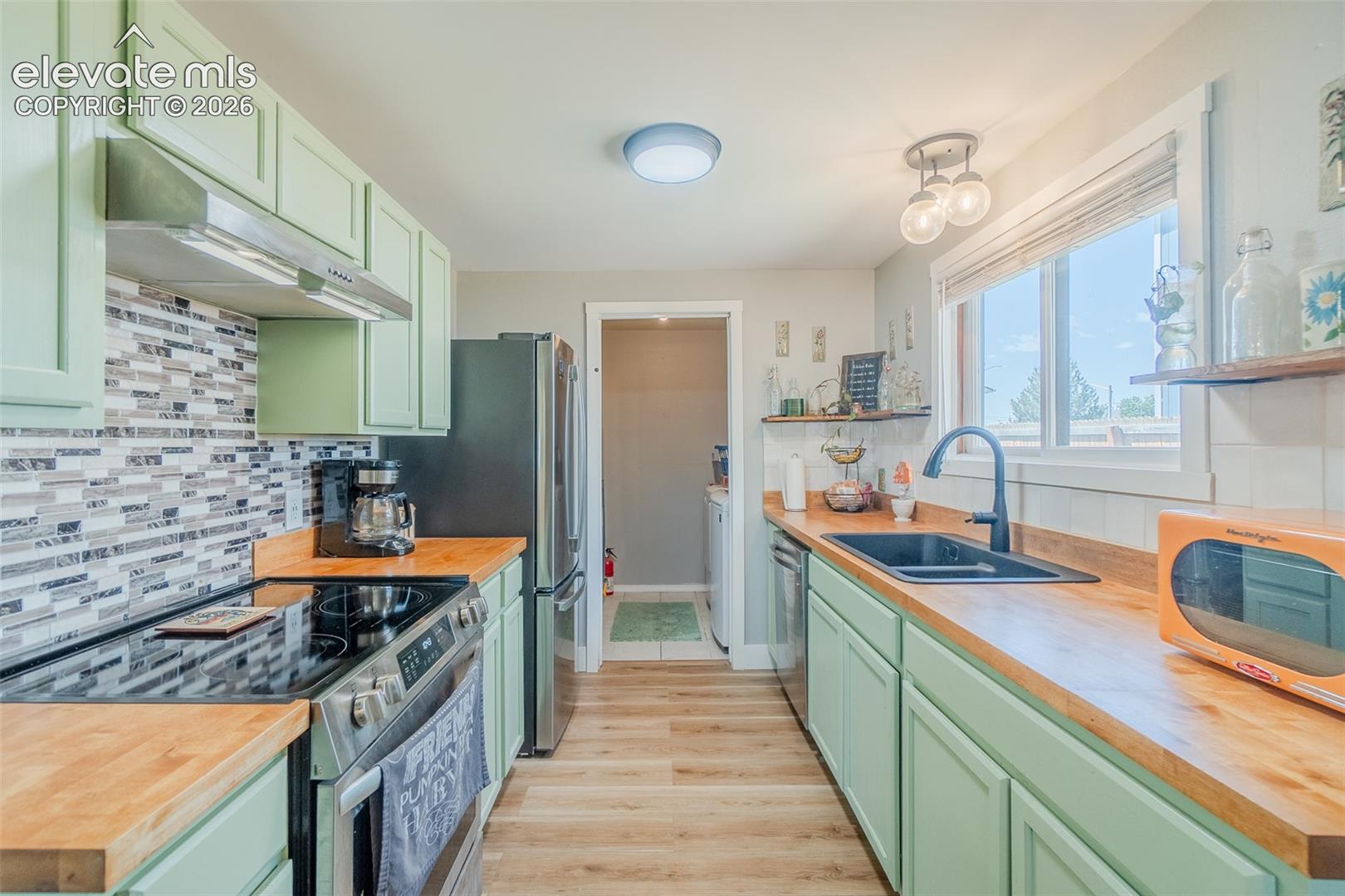 Kitchen featuring mint green cabinetry, wood-finish countertops, stainless steel appliances, a mosaic tile backsplash, and wood-finish flooring