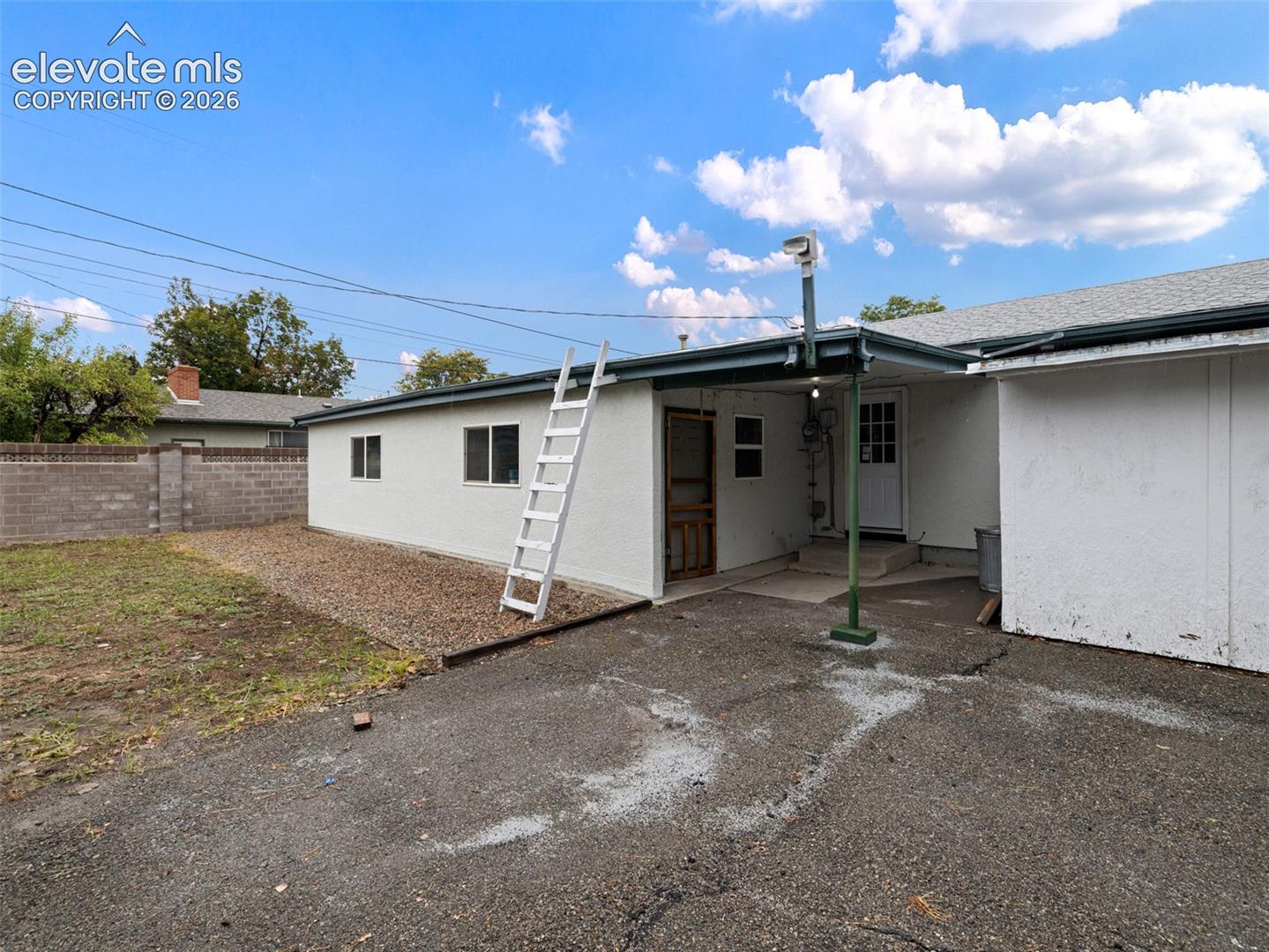 White stucco exterior with multiple windows, covered patio, and concrete block fencing