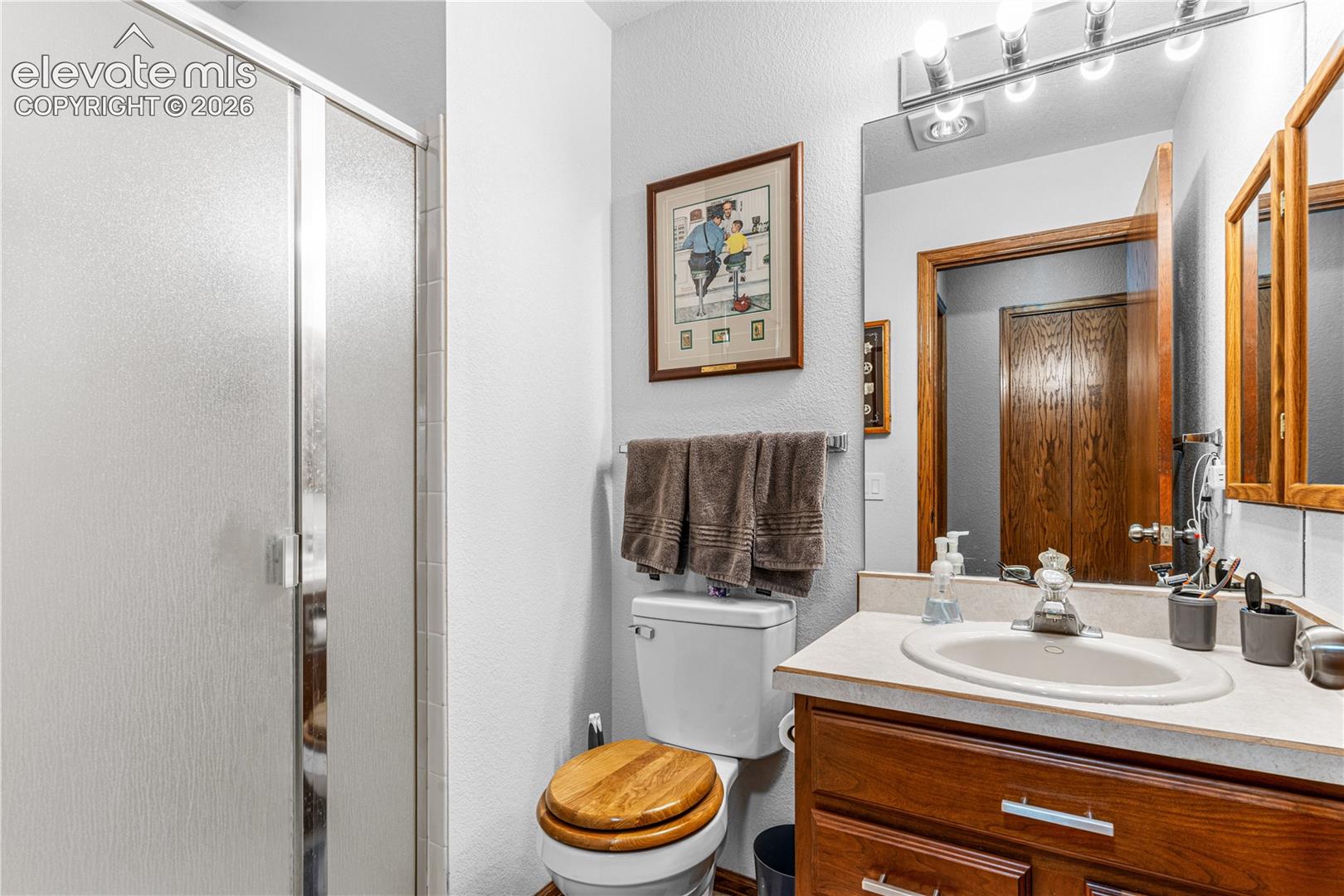 Bathroom featuring a wooden vanity, integrated countertop with a basin sink, chrome faucet, glass-enclosed shower, and large wall-mounted mirror